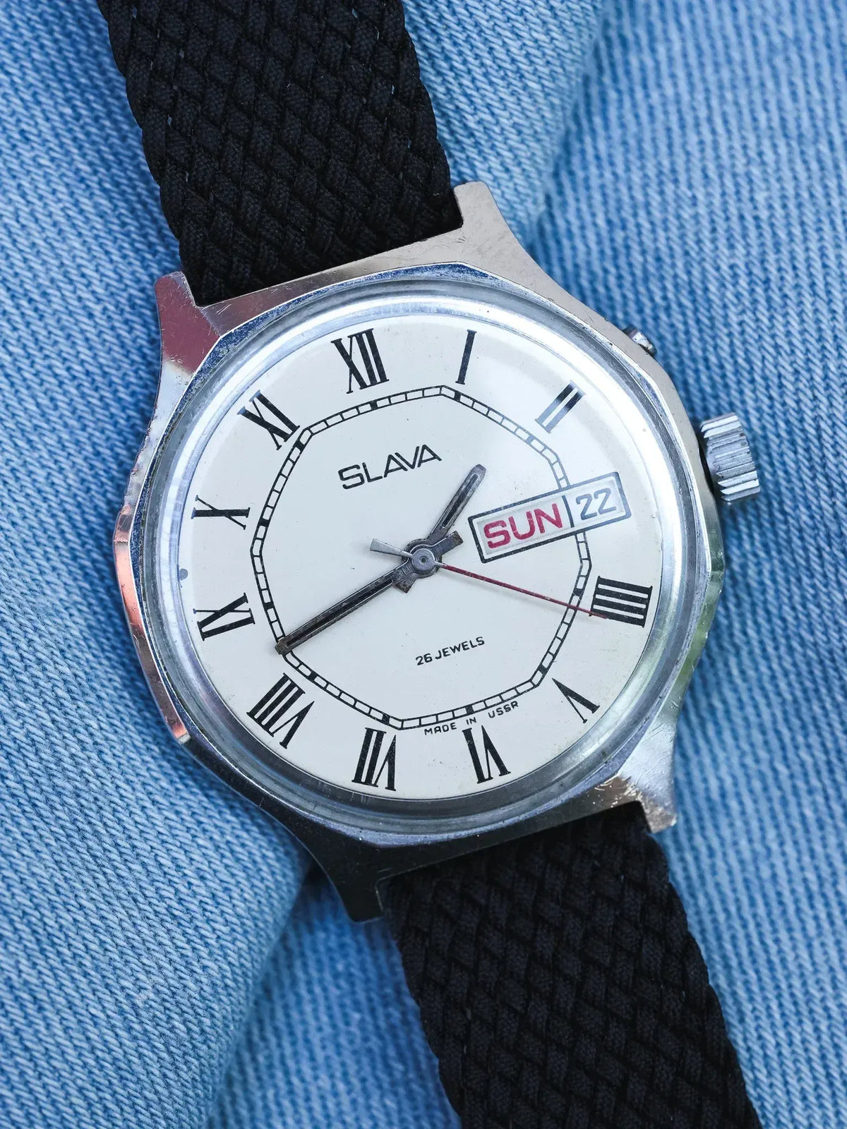 Slava vintage watch with white dial, Roman numerals, day-date, black fabric strap on denim