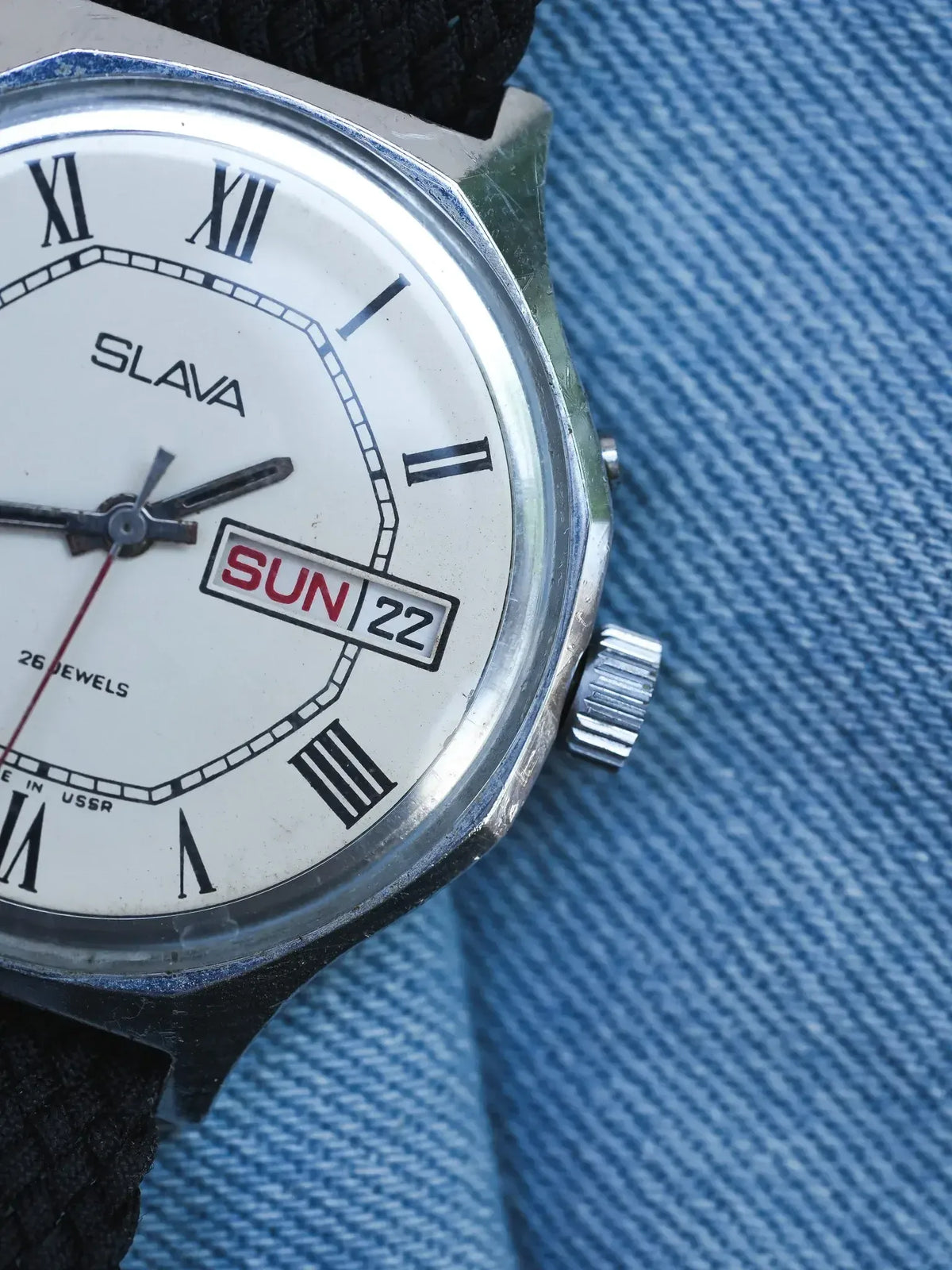 Slava vintage watch with white dial, Roman numerals, day-date display, on denim background