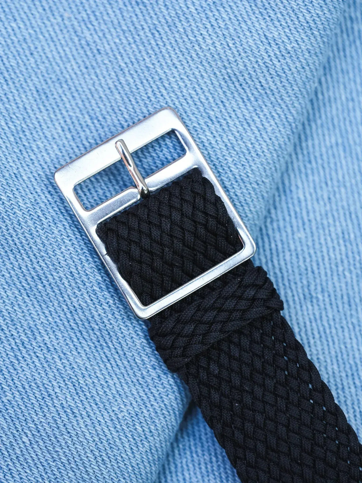 Black braided fabric watch strap with silver buckle on blue denim