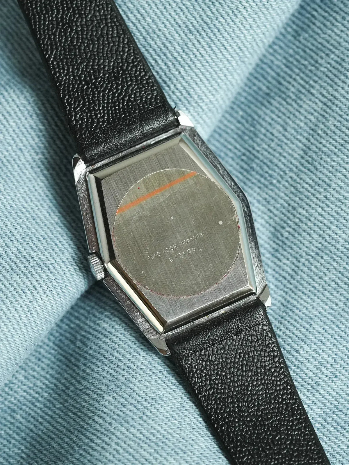 Vintage Omega watch with stainless steel case and black leather strap, back view on fabric