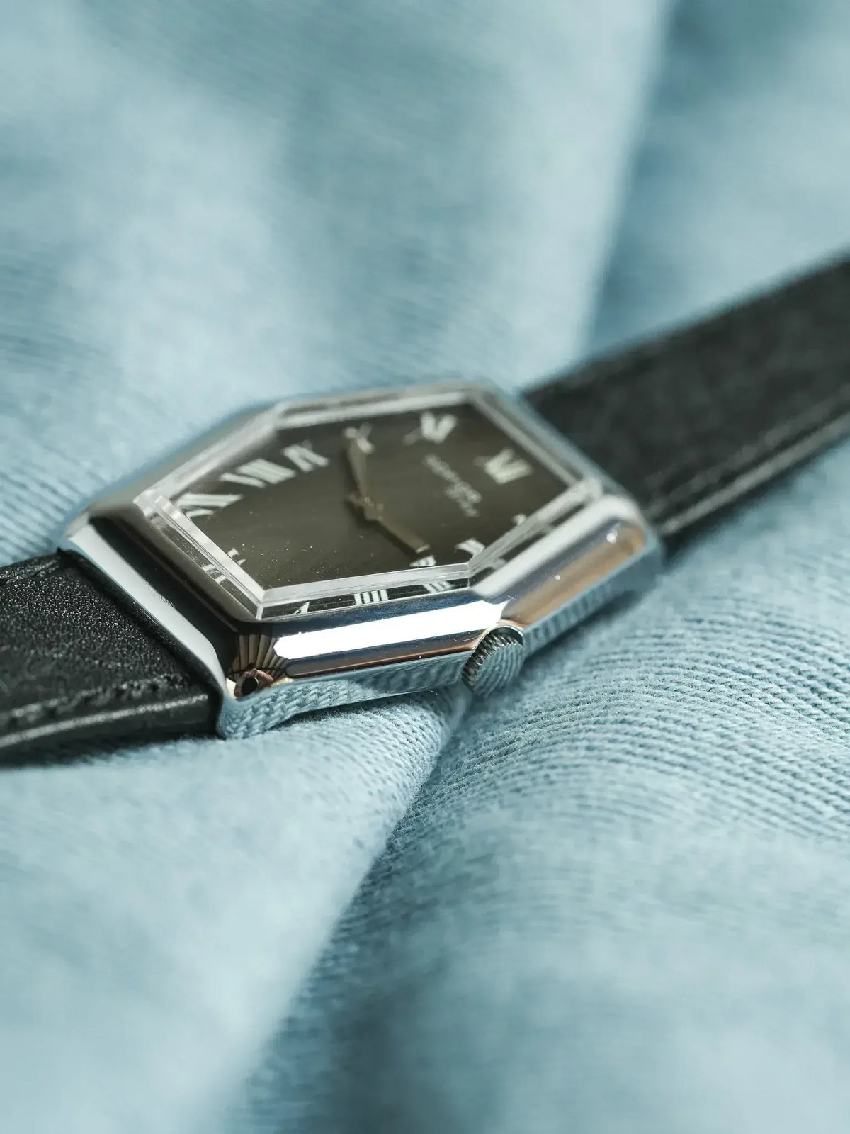 Cartier vintage watch with octagonal case, black dial, Roman numerals, black leather strap on blue fabric