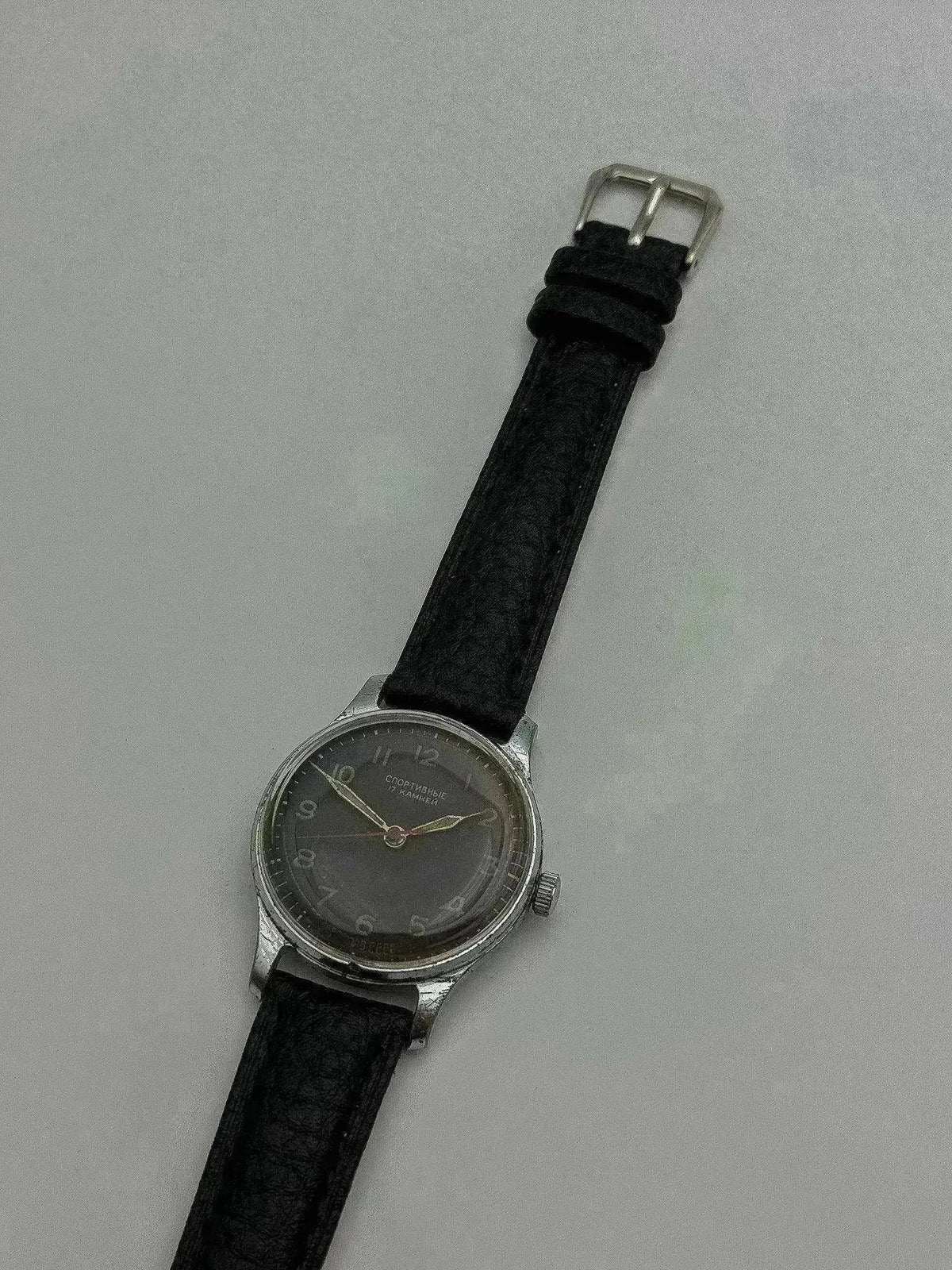 Vintage Soviet Sportivnye watch with gray dial, black leather strap, steel case on neutral background