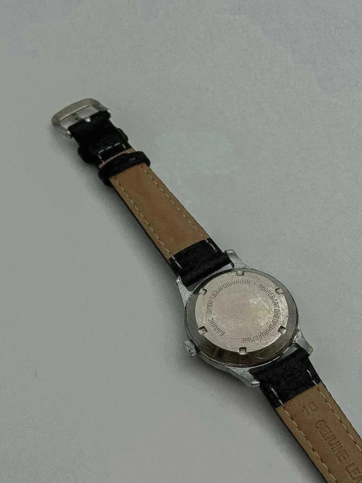 Vintage Vostok watch with steel case, black leather strap, displayed back view on neutral background