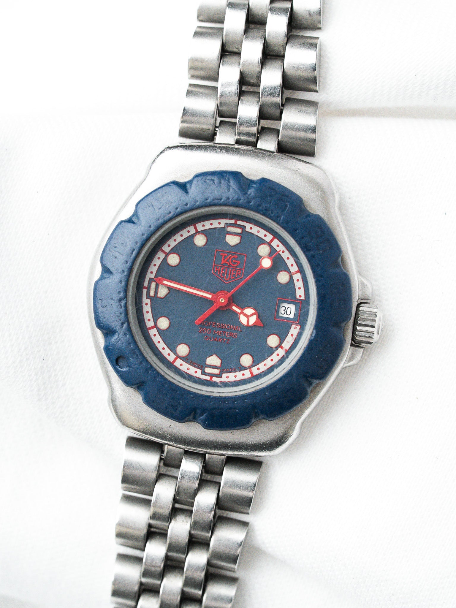 TAG Heuer vintage watch with blue dial, red hands, steel bracelet, and scalloped bezel