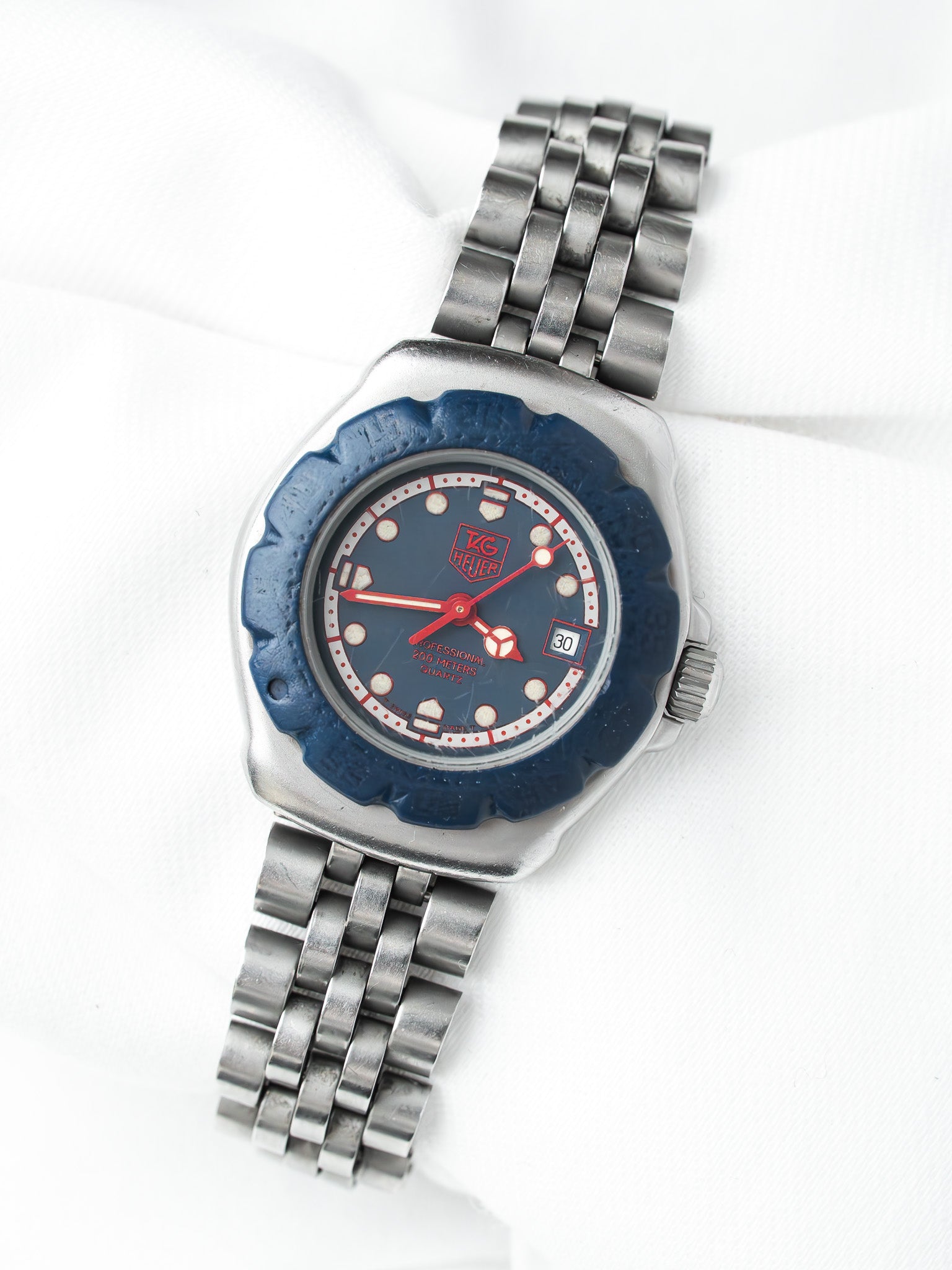 TAG Heuer vintage watch with blue dial, red hands, steel bracelet on white background