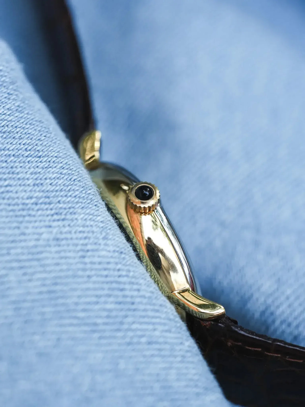 Vintage Cartier watch with gold case, black cabochon crown, brown leather strap on blue fabric