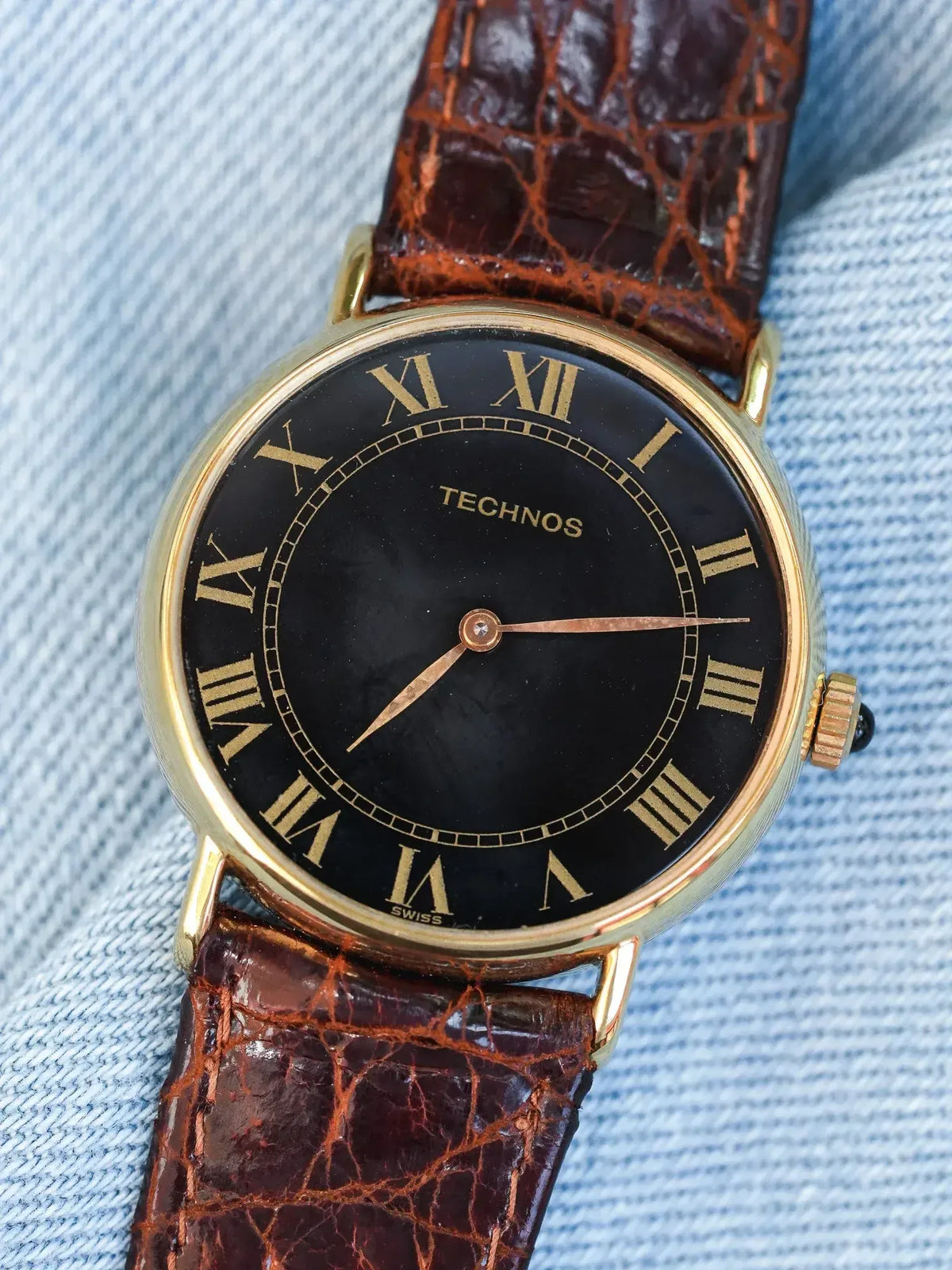 Technos vintage watch with black dial, gold Roman numerals, brown alligator strap on denim
