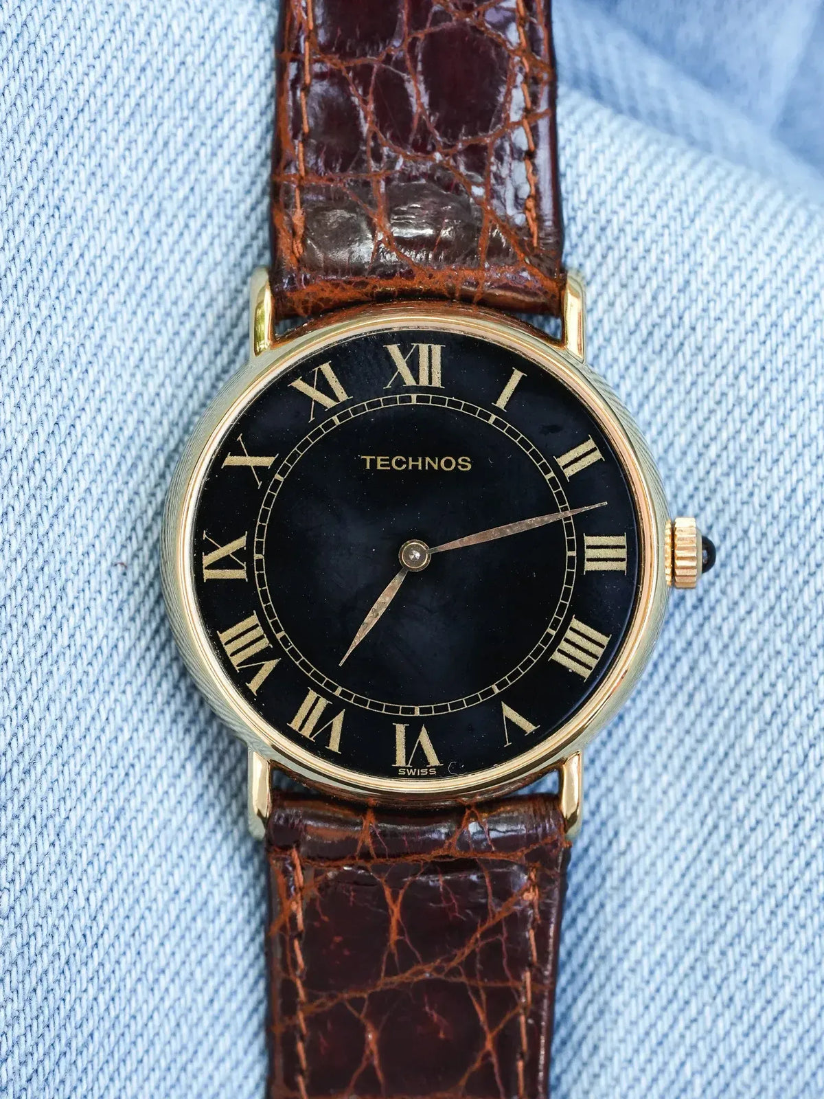 Technos vintage watch with black dial, gold Roman numerals, brown alligator strap on denim