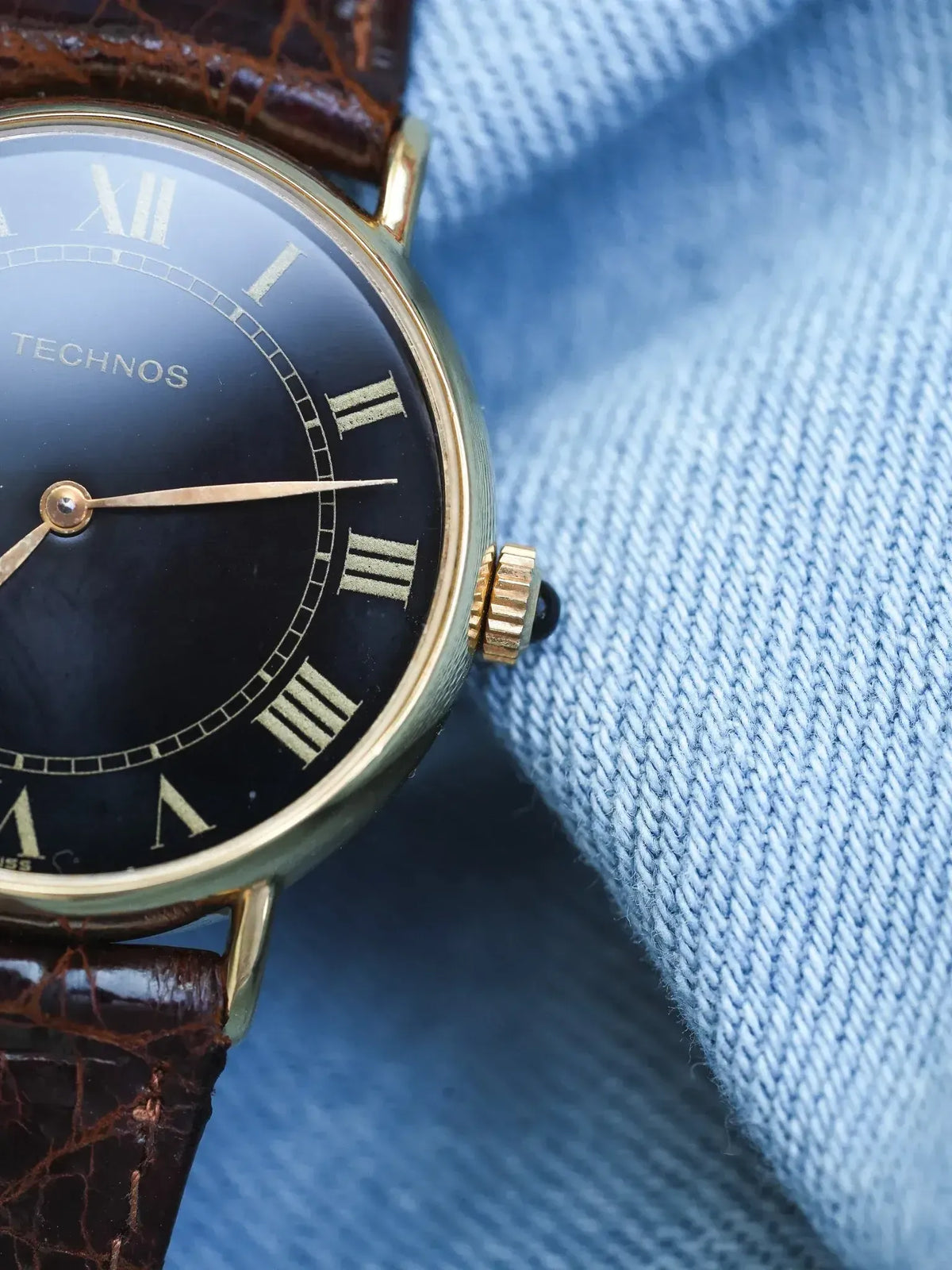 Technos vintage watch with black dial, gold case, Roman numerals, brown leather strap on denim