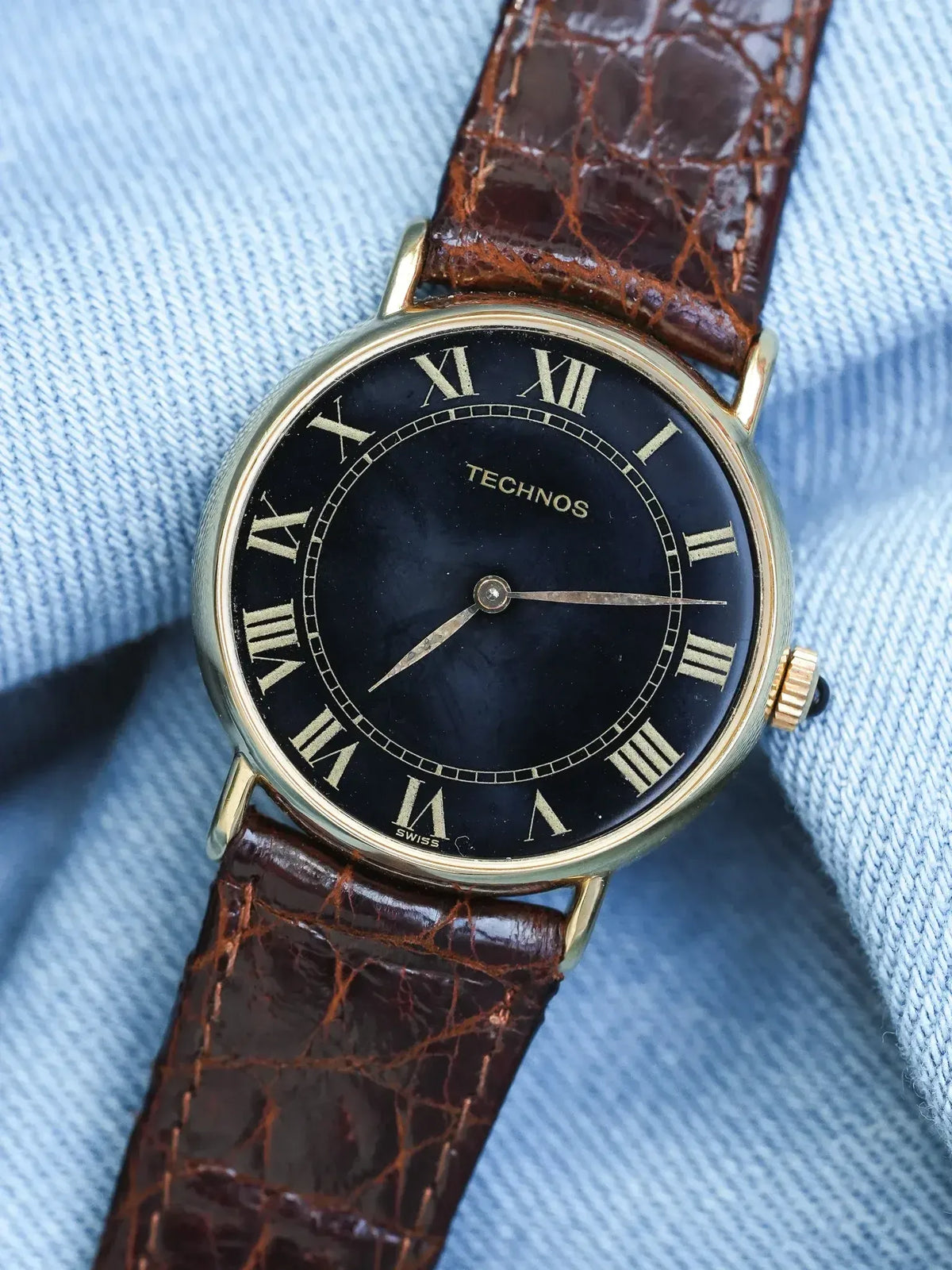 Technos vintage watch with black dial, gold case, and brown alligator strap on denim