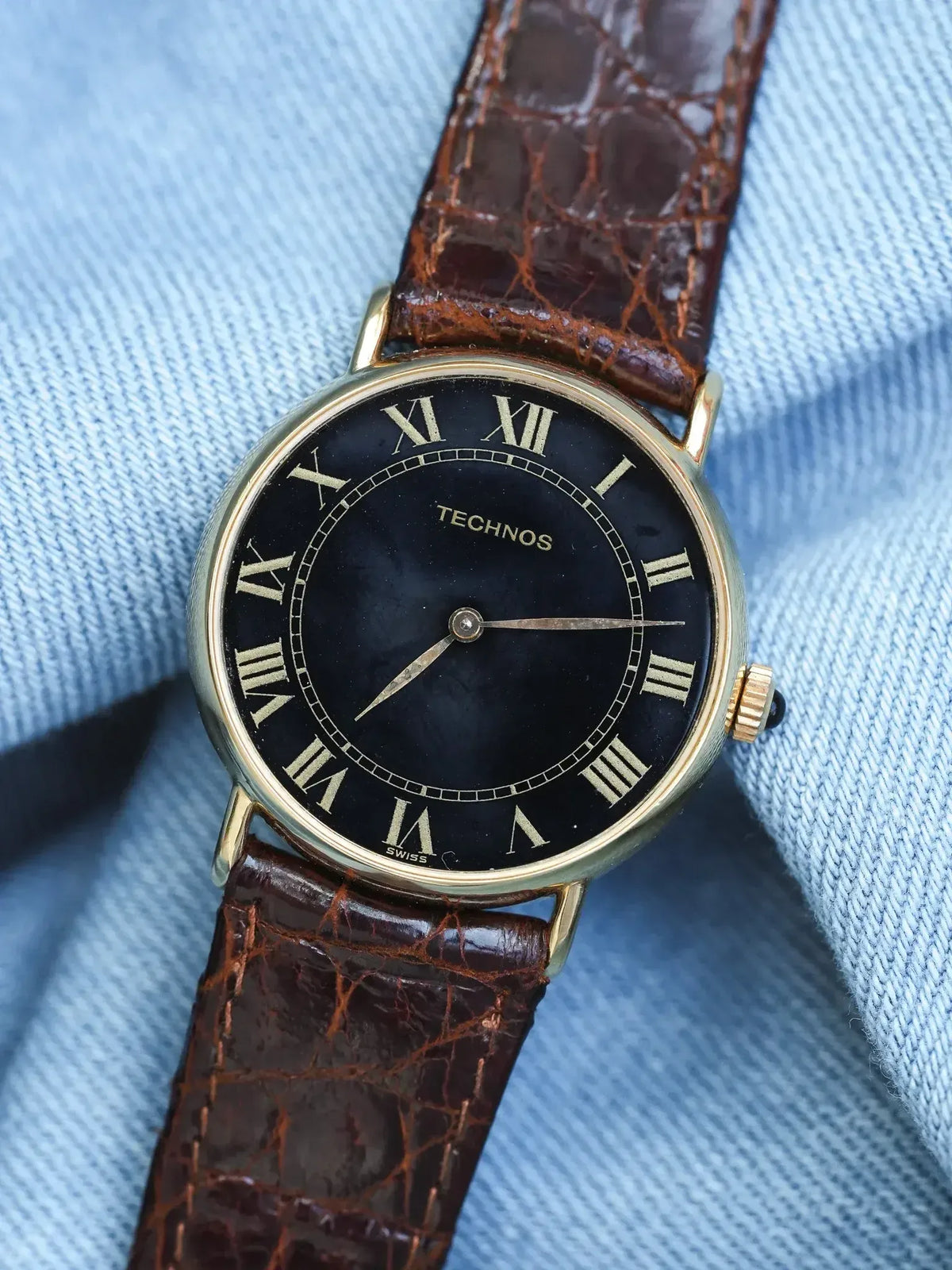 Technos vintage watch with black dial, gold case, brown alligator strap on denim