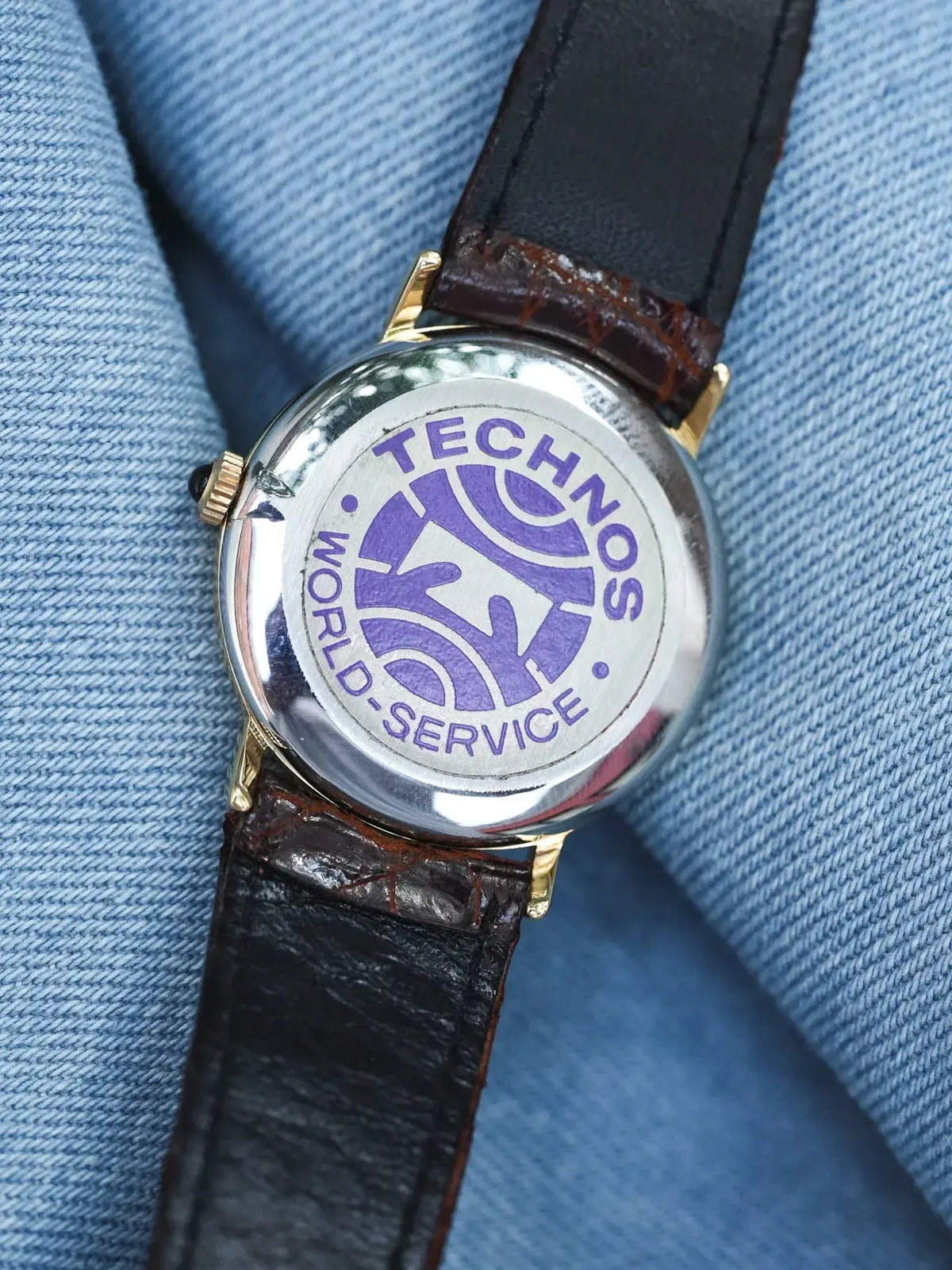 Technos vintage watch back with purple logo, gold case, brown leather strap on denim