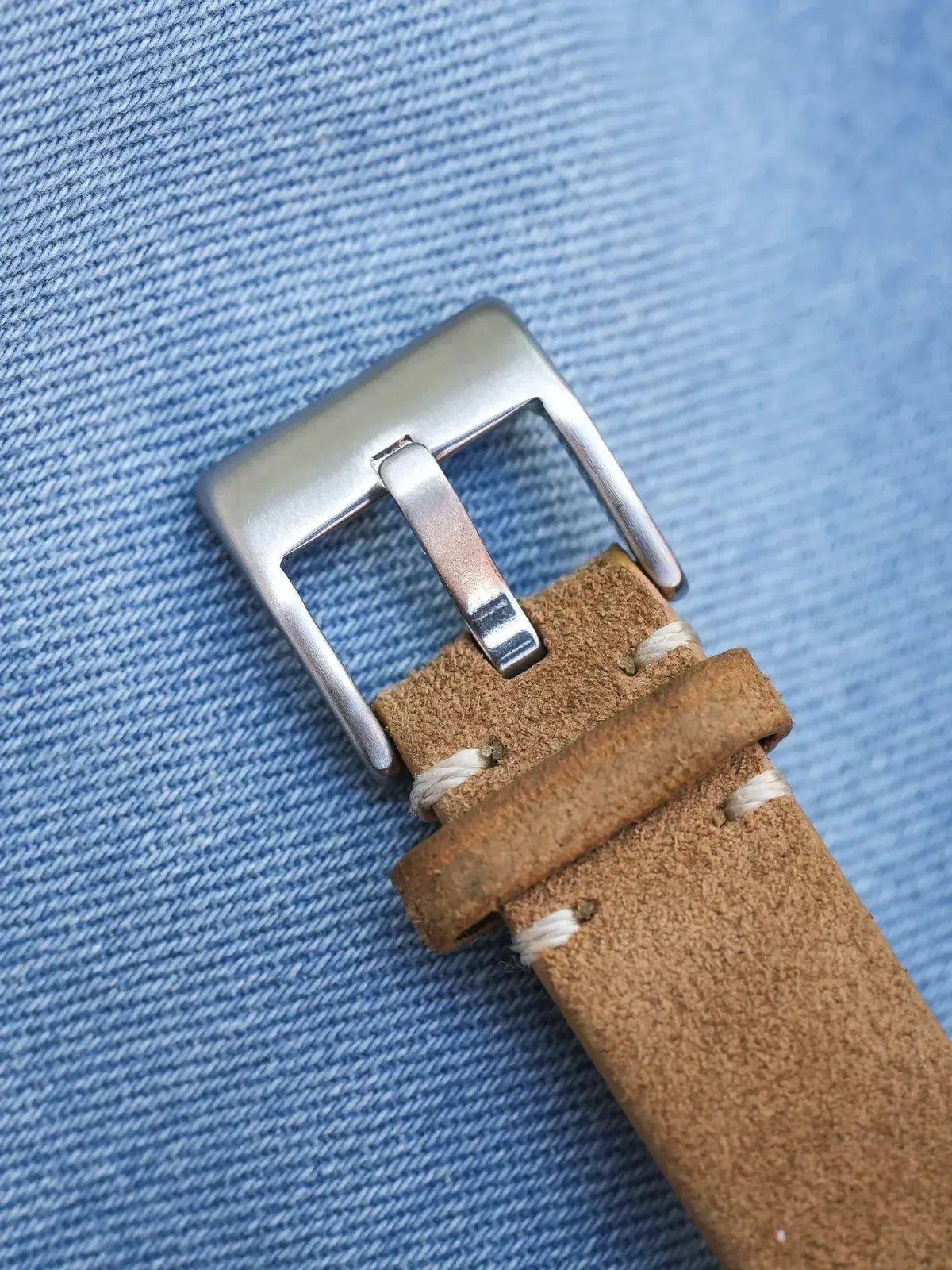 Vintage watch strap in tan suede with white stitching and silver buckle on denim