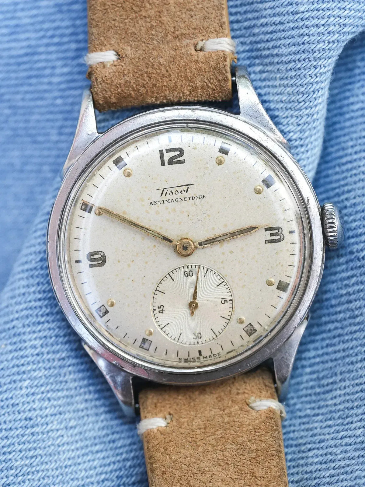 Vintage Tissot Antimagnetique watch with cream dial, steel case, brown leather strap on denim