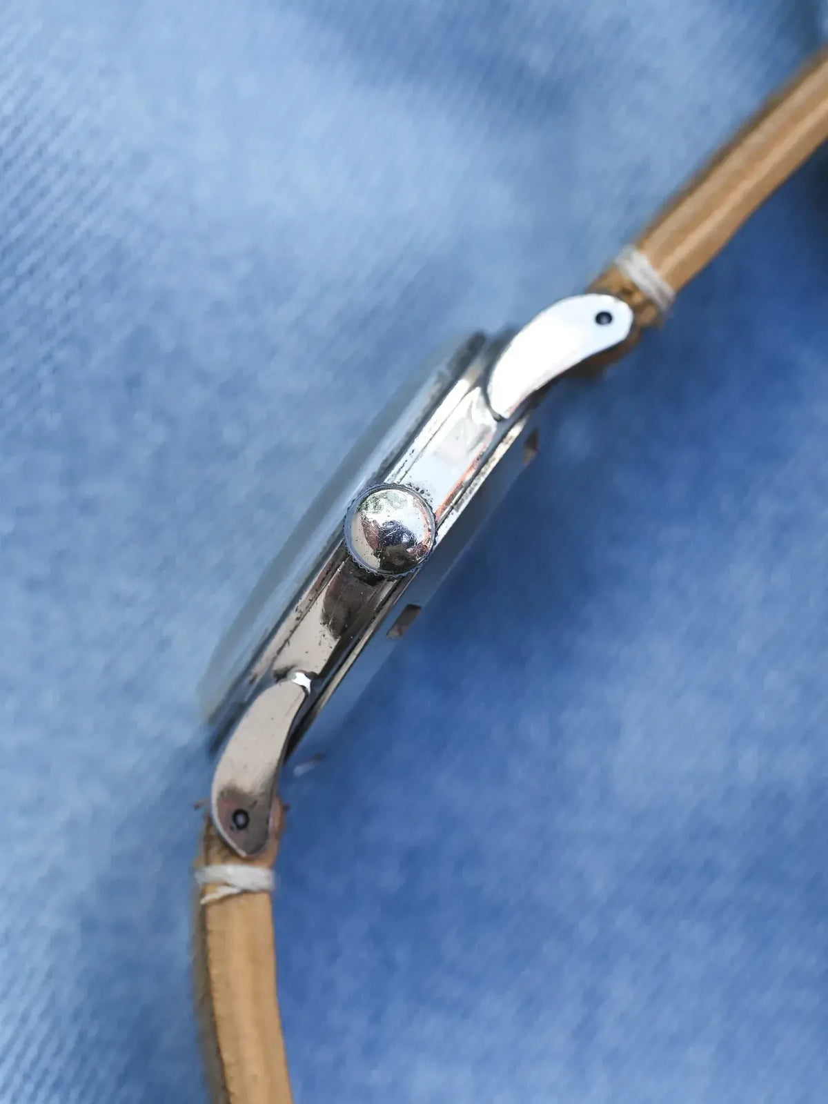 Vintage watch side view with polished steel case and tan leather strap on blue fabric