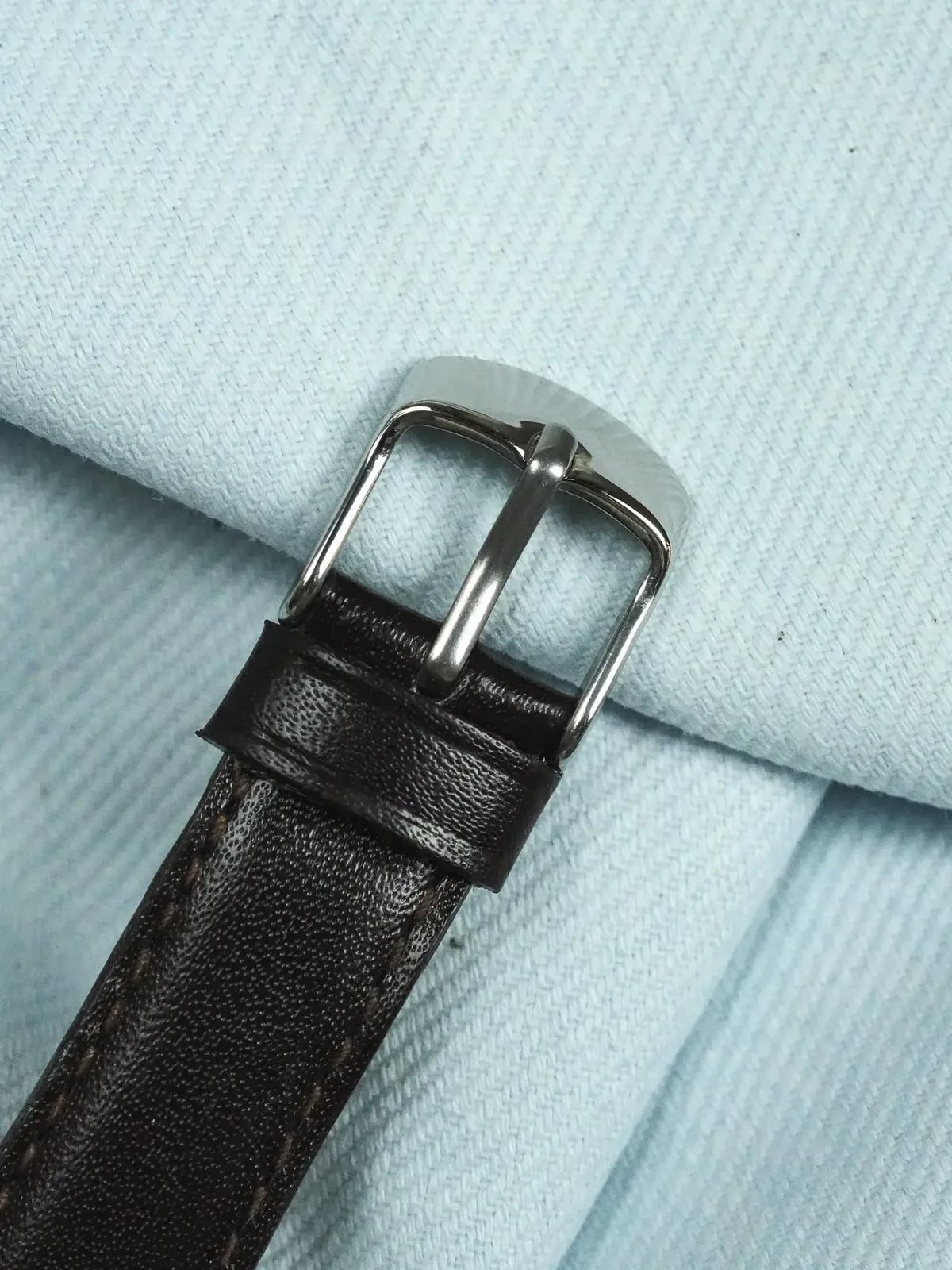 Brown leather watch strap with silver buckle on light blue fabric background