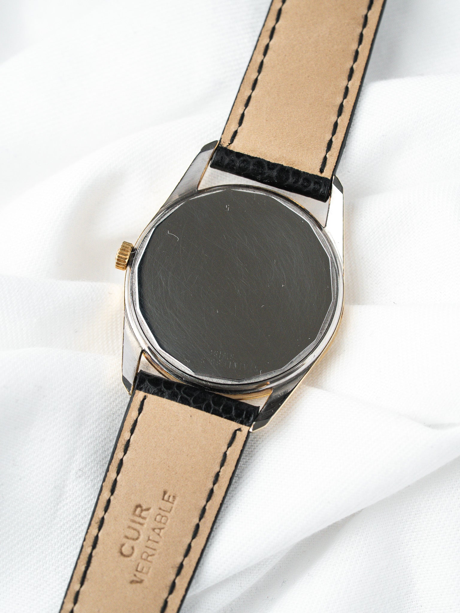 Vintage watch with stainless steel case, gold crown, black leather strap on white fabric