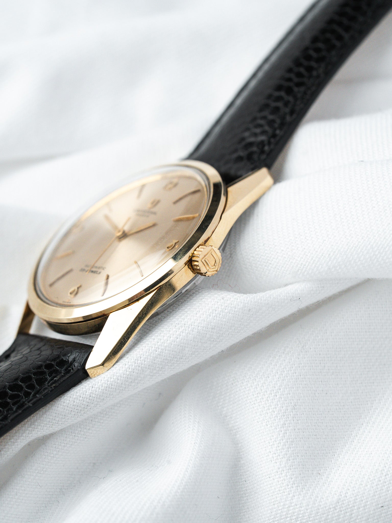 Vintage Omega watch with gold case, cream dial, black lizard strap on white fabric