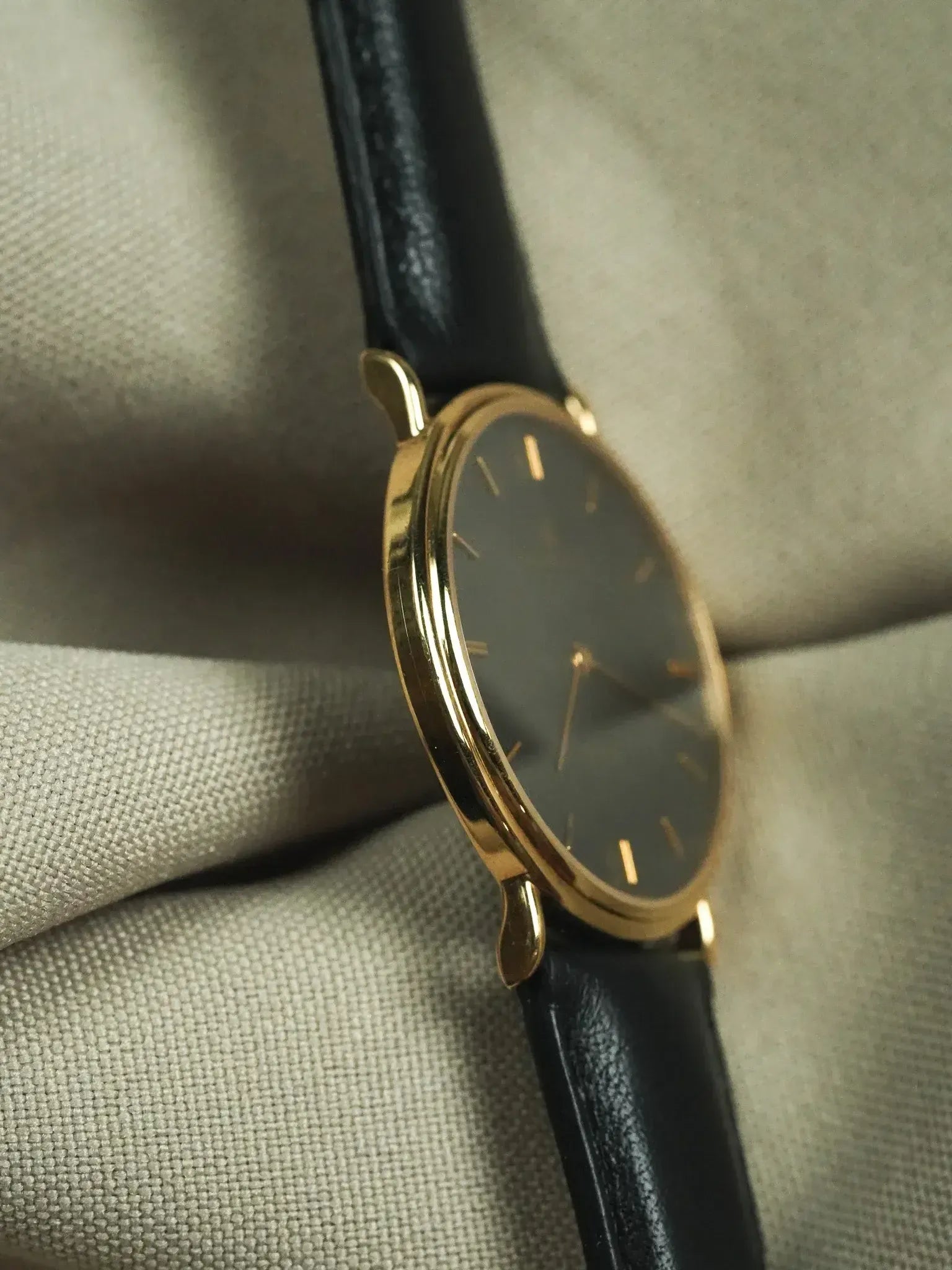 Vintage gold watch with black dial and leather strap on fabric