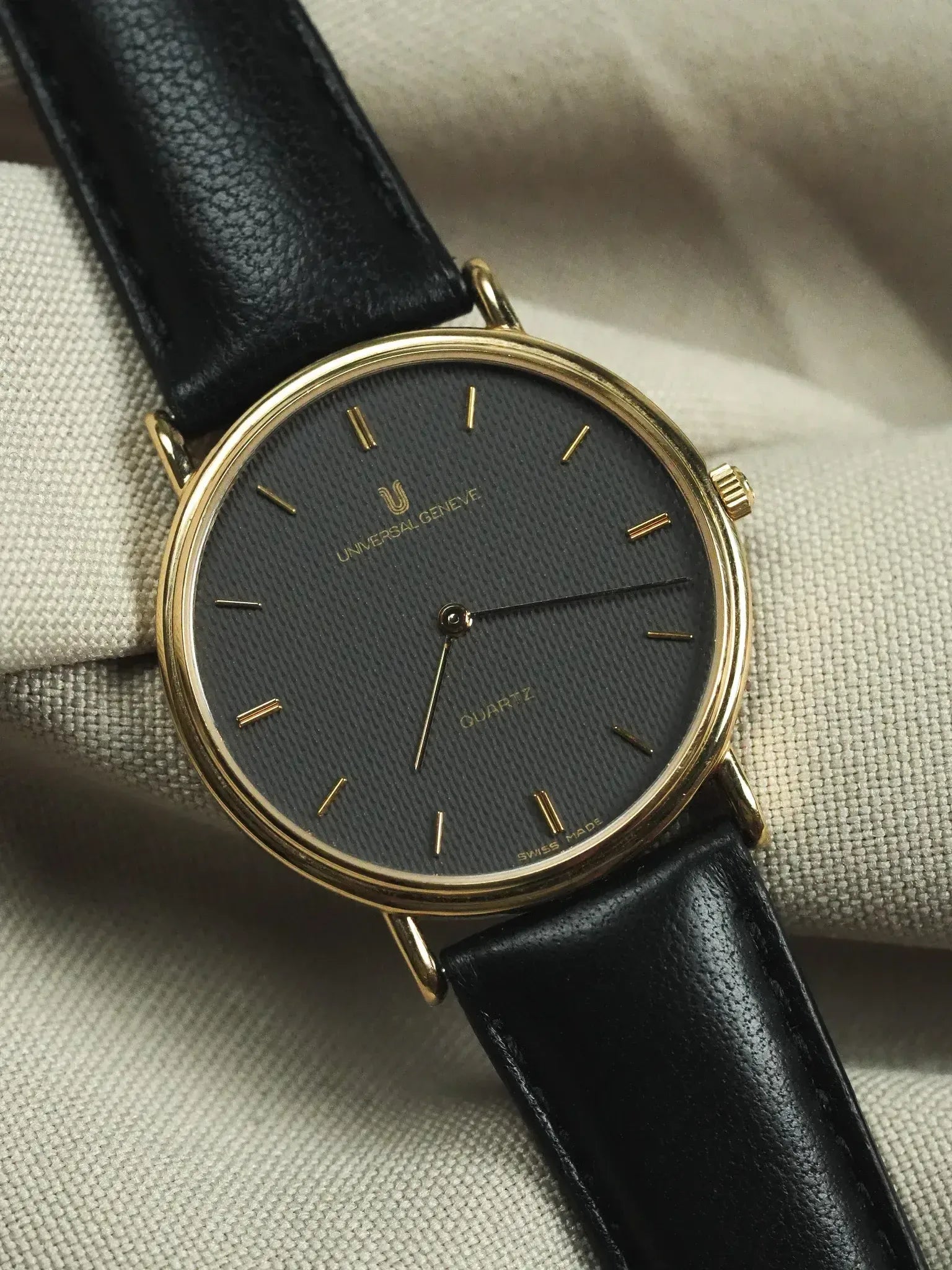 Universal Geneve vintage watch with gold case, black textured dial, and black leather strap