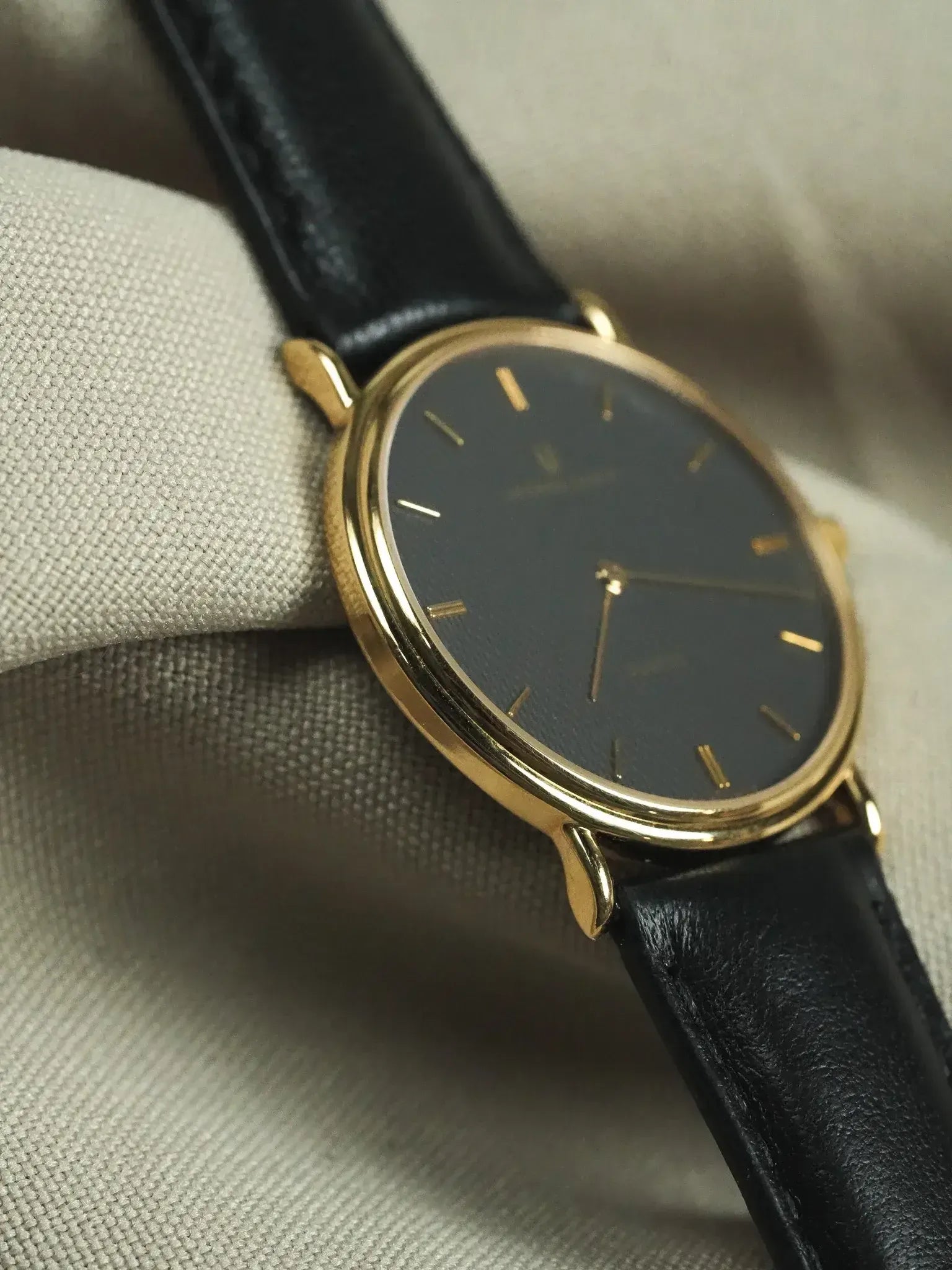 Vintage Omega watch with gold case, black dial, and black leather strap