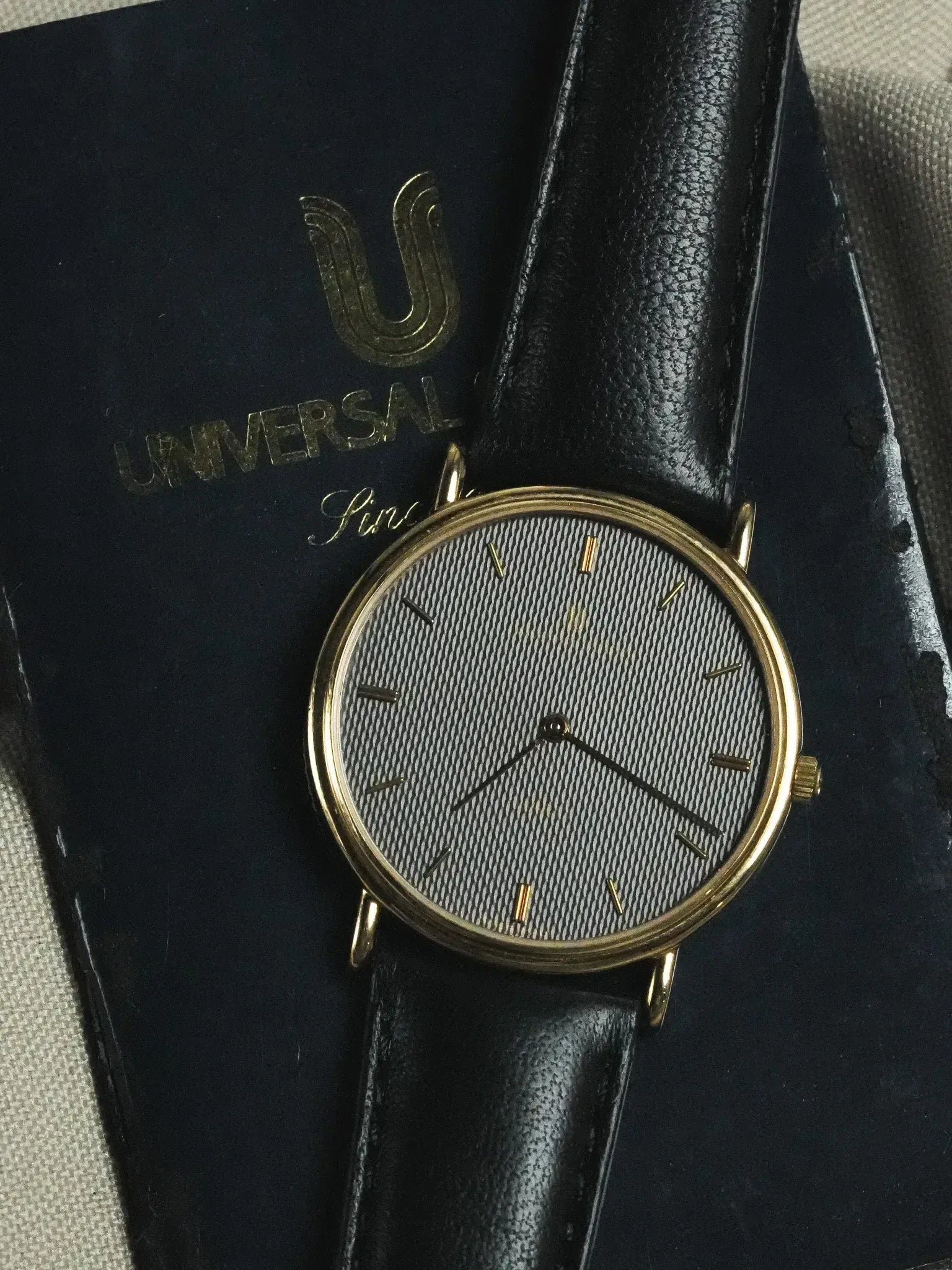 Universal Genève vintage watch with gold case, textured grey dial, black leather strap