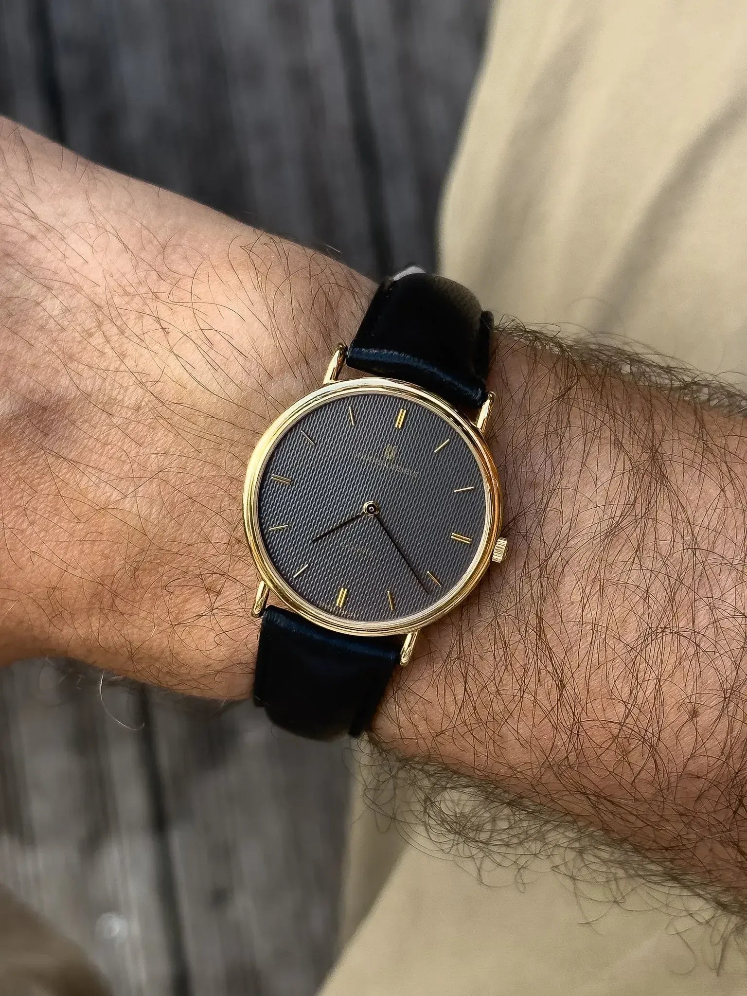 Universal Genève vintage watch with gold case, grey textured dial, black leather strap on wrist