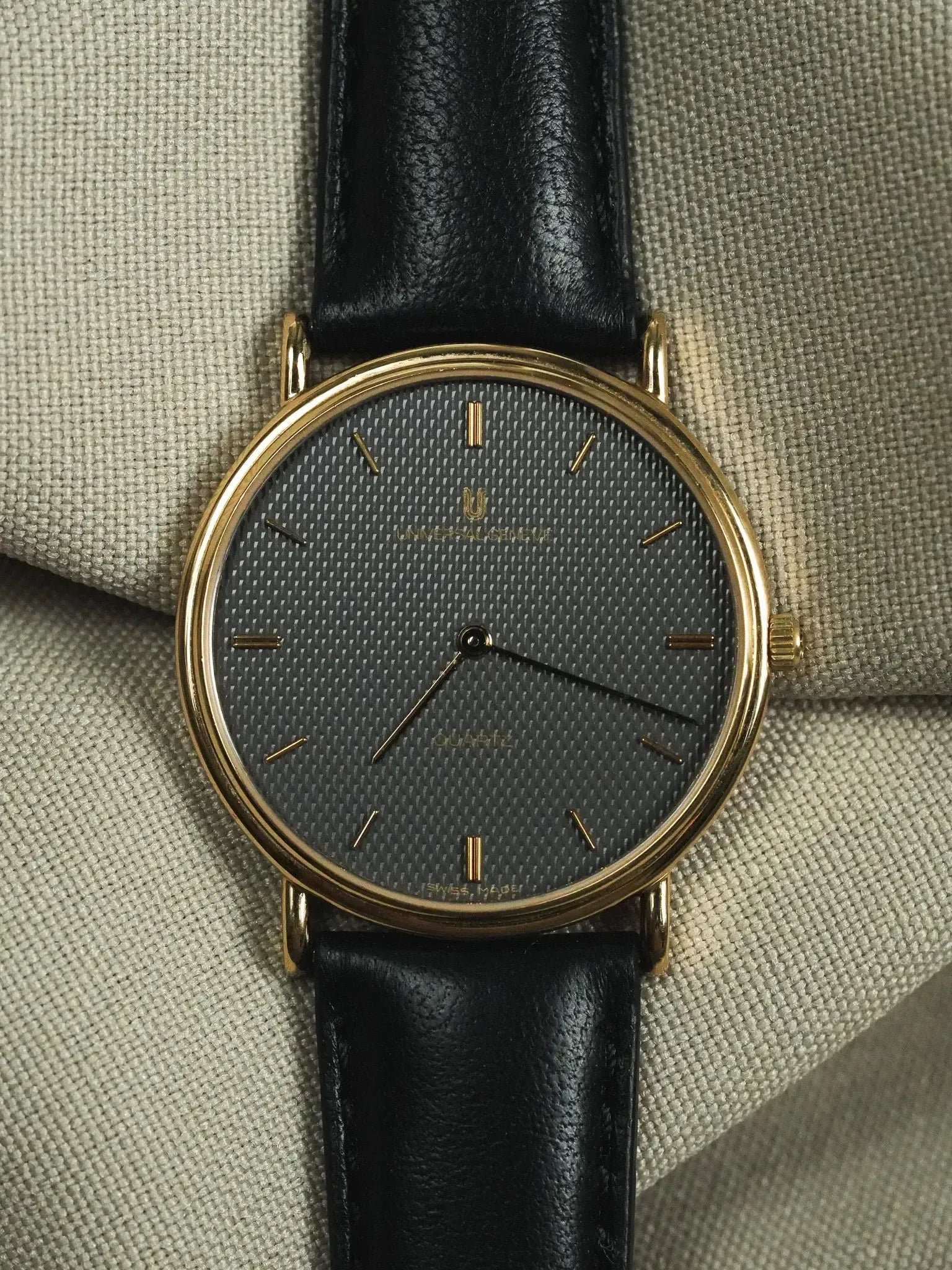 Universal Genève vintage watch with gold case, grey textured dial, black leather strap