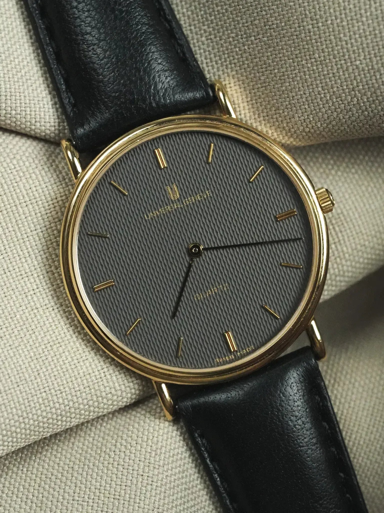 Universal Genève vintage watch with gold case, grey textured dial, black leather strap