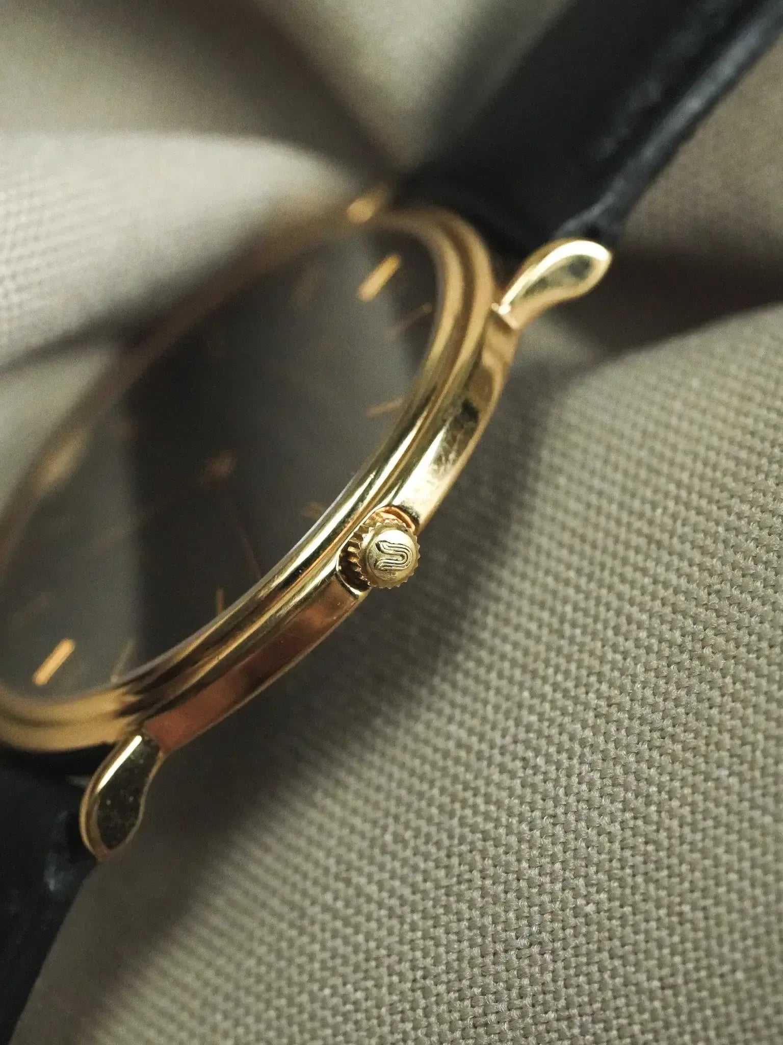 Vintage Universal Genève watch with gold case, black dial, and black leather strap