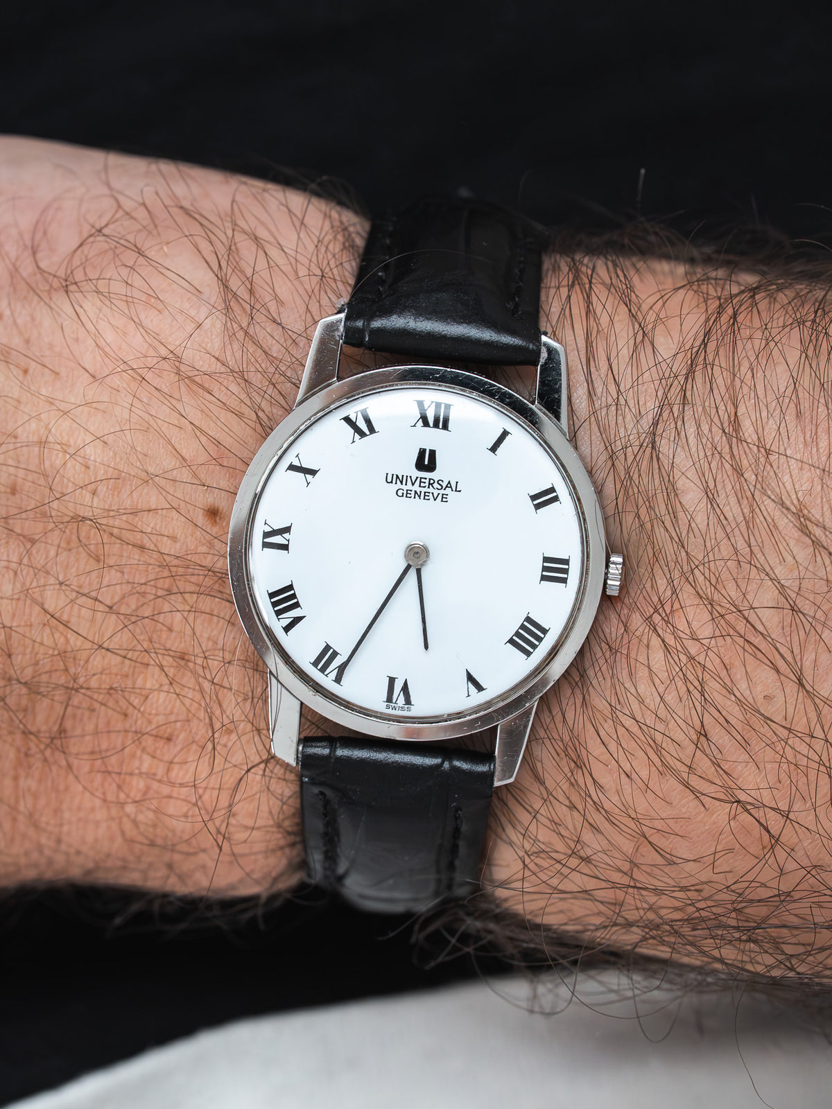 Universal Geneve vintage watch with white dial, Roman numerals, black leather strap on wrist