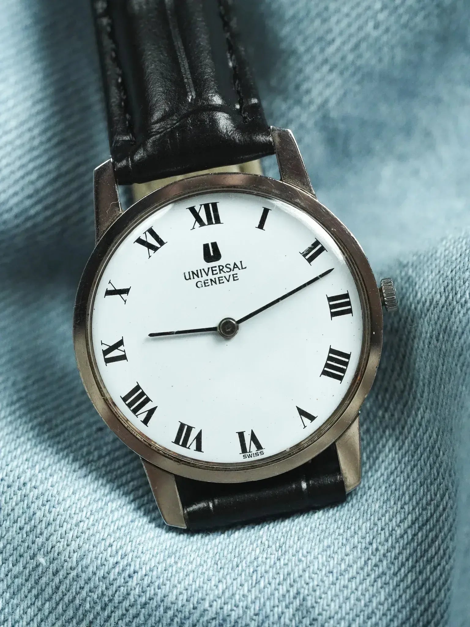 Universal Geneve vintage watch with white dial, Roman numerals, black leather strap on denim