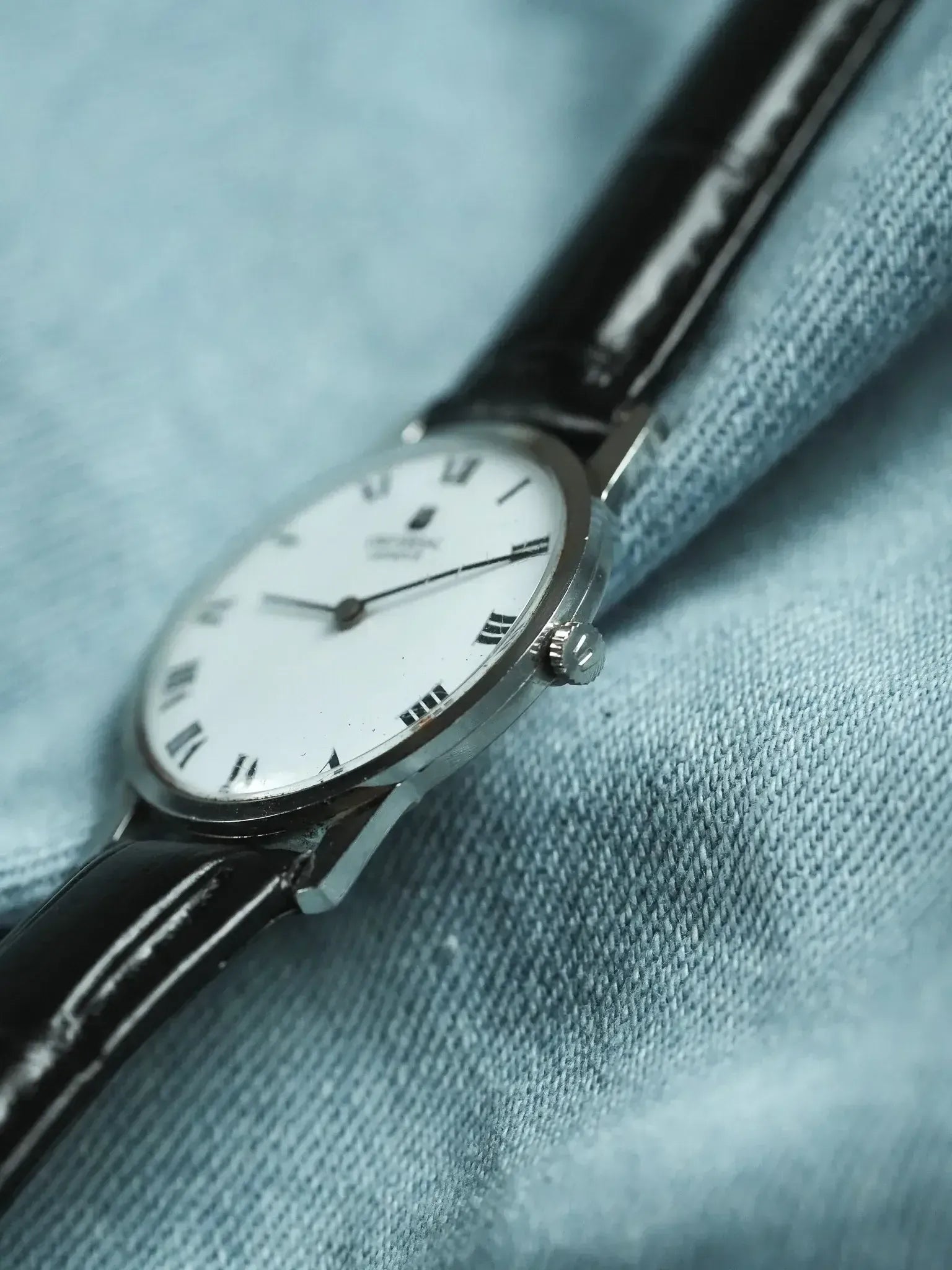 Vintage Omega watch with white dial, Roman numerals, black leather strap on denim