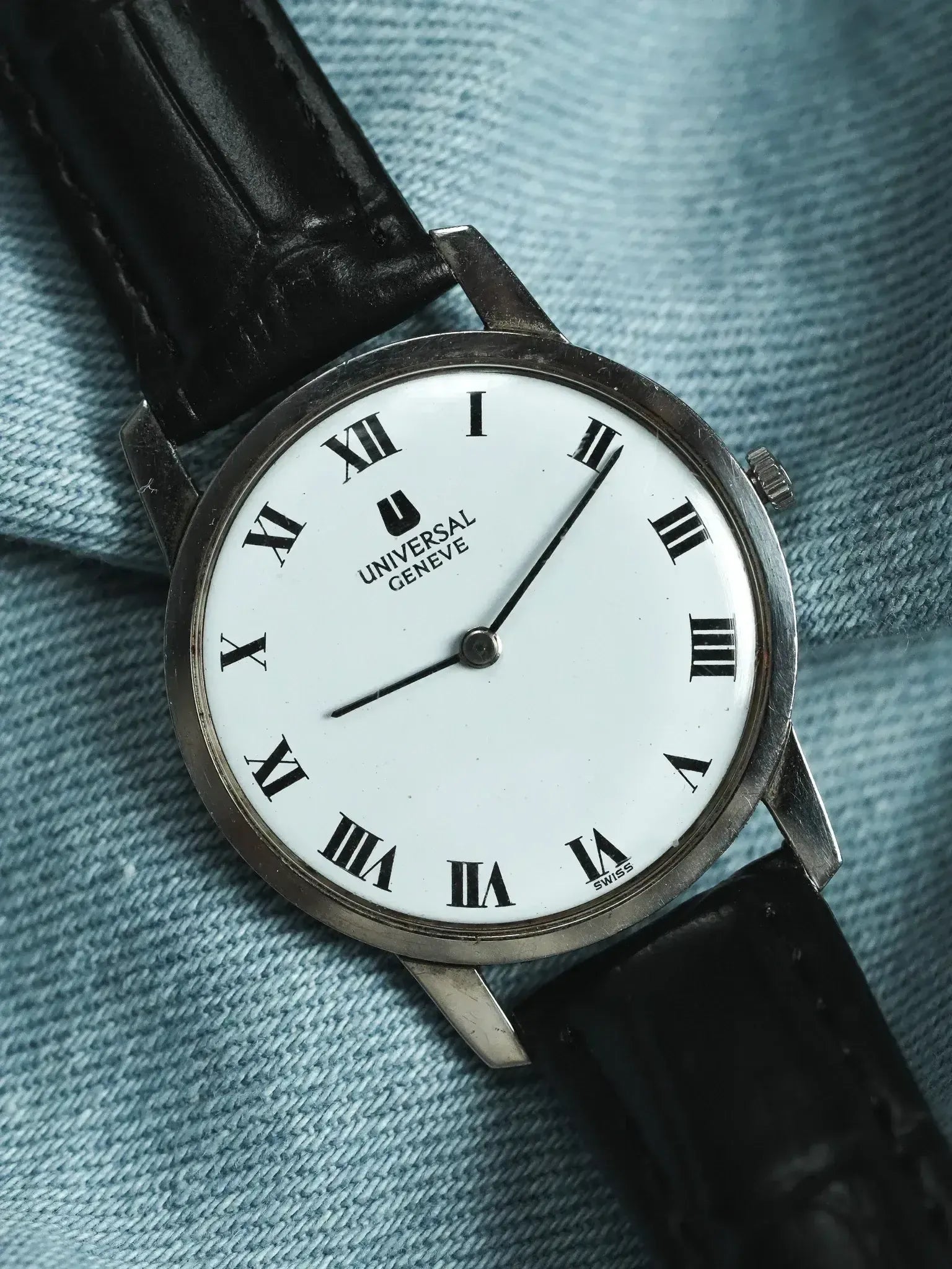 Universal Geneve vintage watch with white dial, Roman numerals, black leather strap on denim