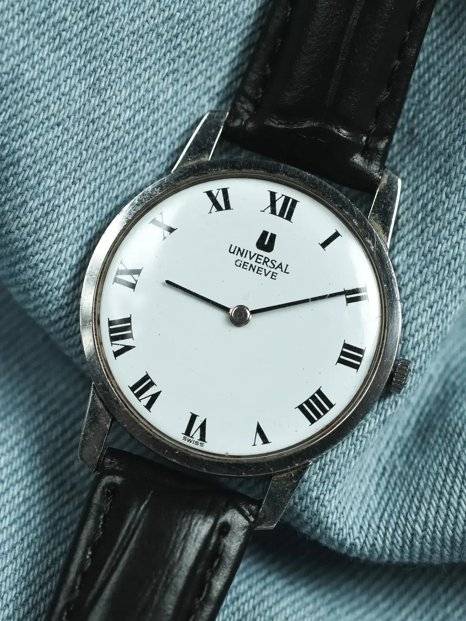 Universal Geneve vintage watch with white dial, Roman numerals, black leather strap on denim