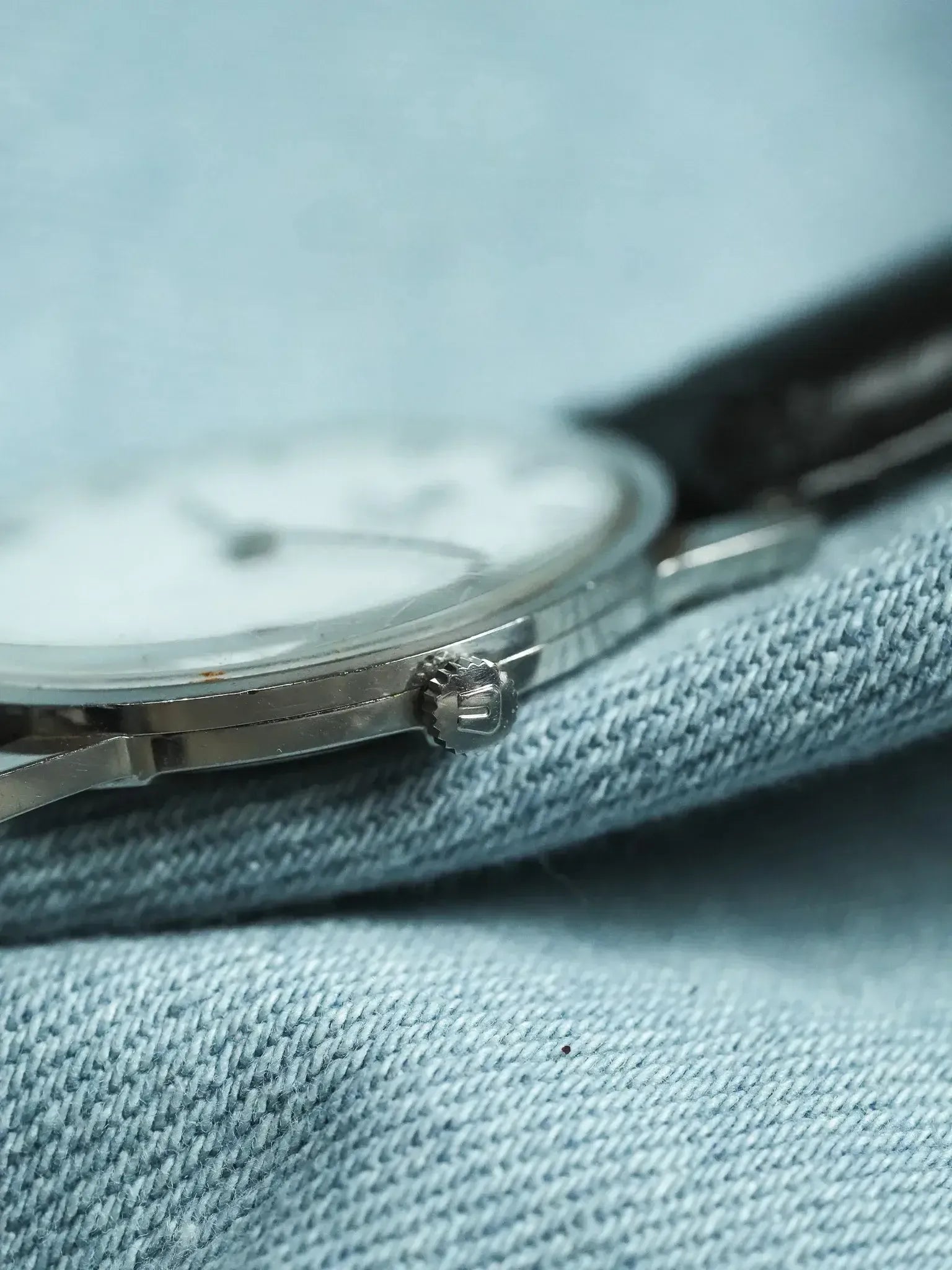 Vintage Rolex watch with silver case and white dial on denim fabric