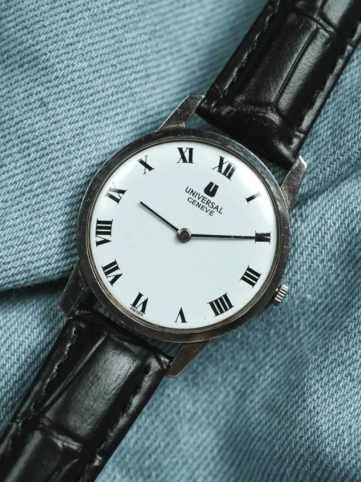 Universal Geneve vintage watch with white dial, Roman numerals, black leather strap on denim