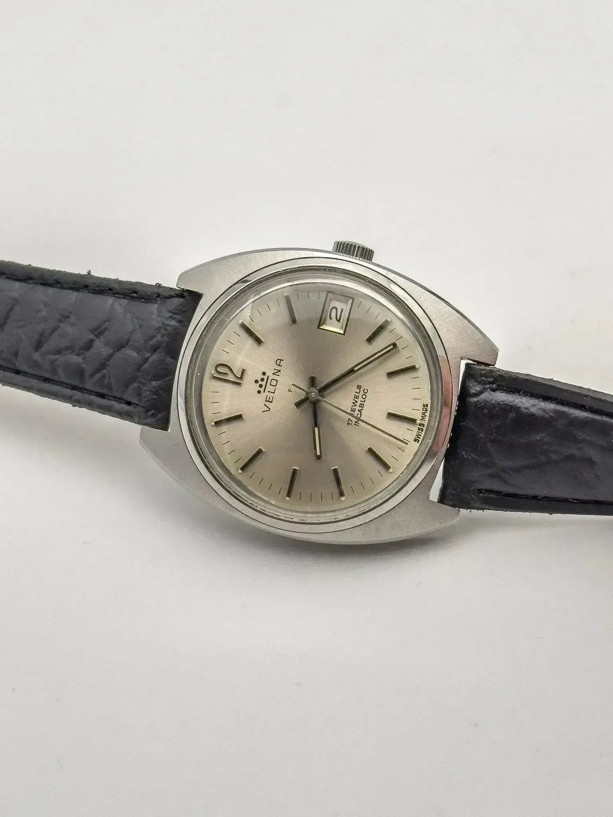 Velona vintage watch with silver dial, black leather strap, date window, on white background