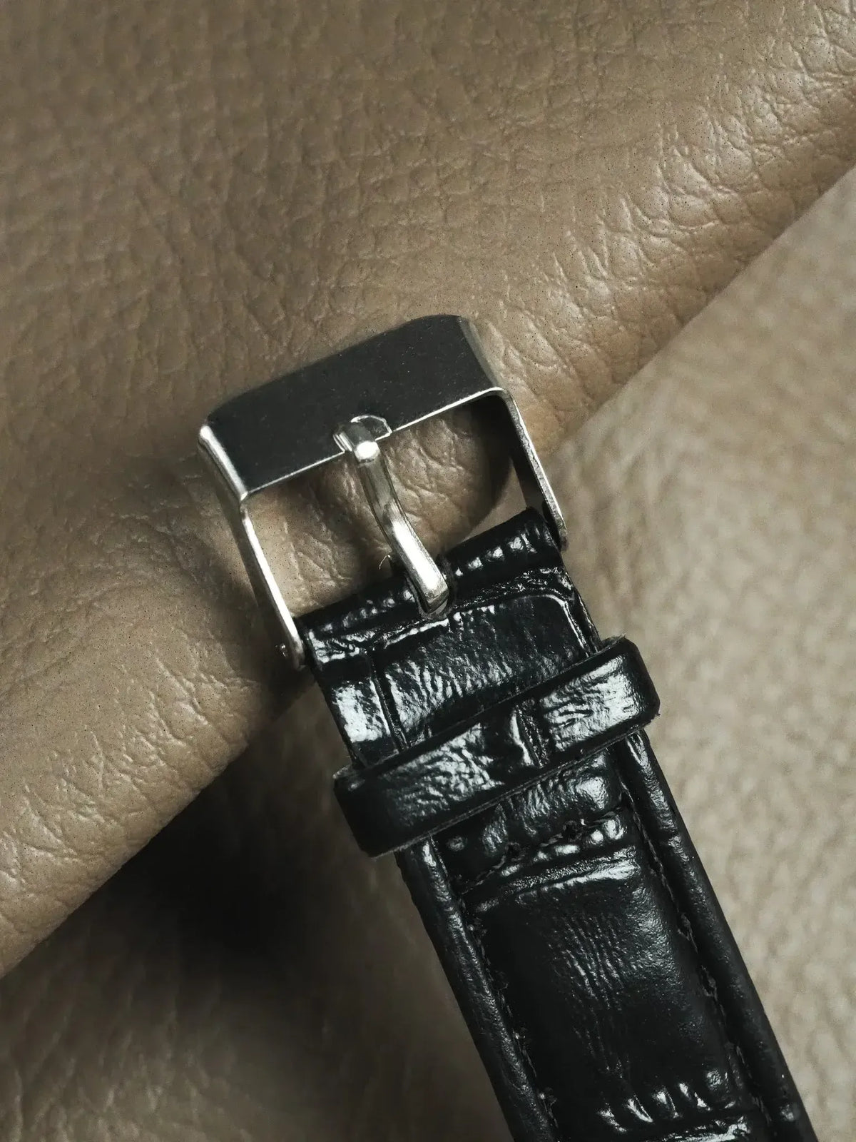 Black alligator leather watch strap with polished steel buckle on textured surface