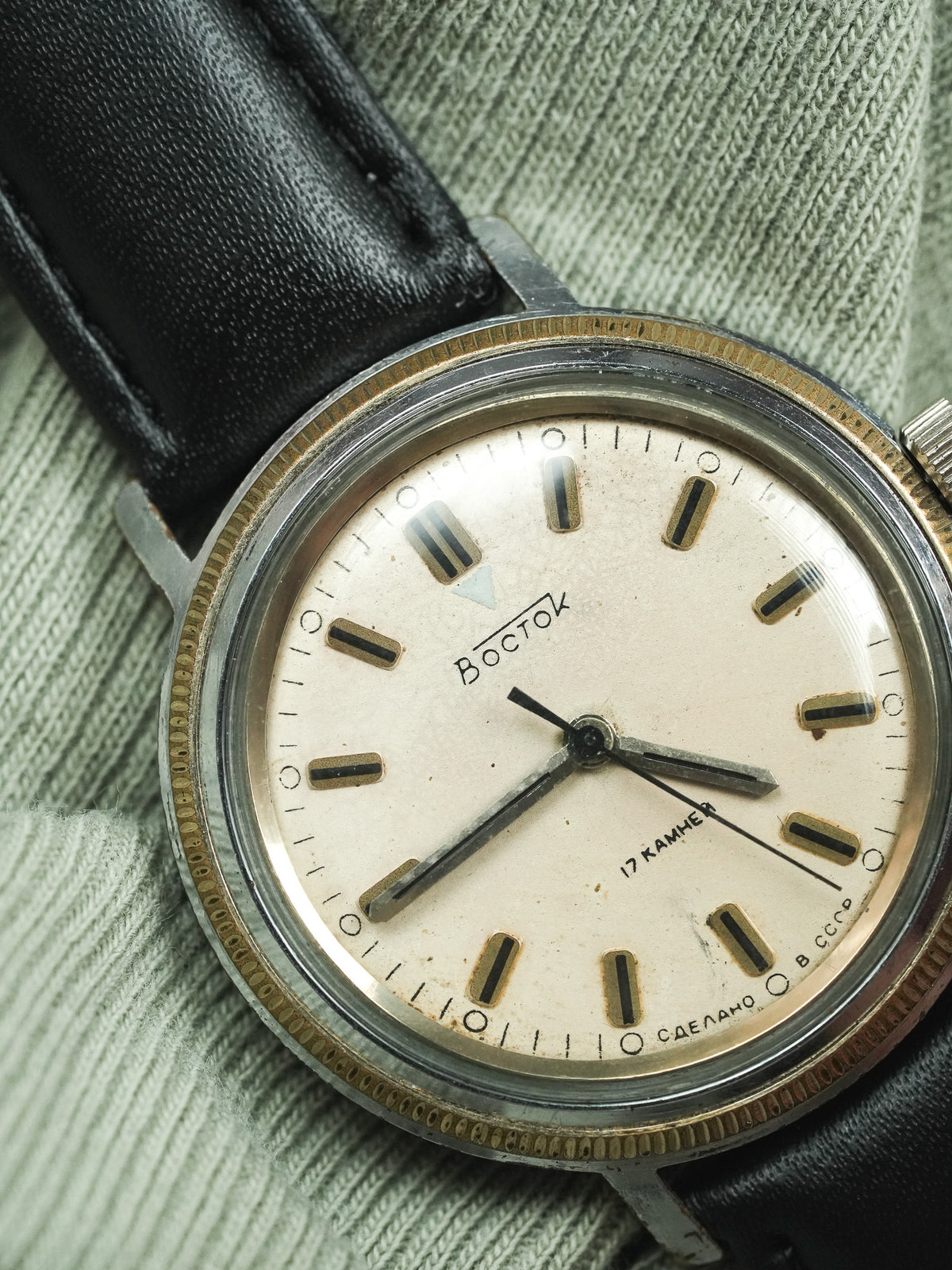 Vintage Vostok watch with cream dial, black leather strap, resting on green fabric