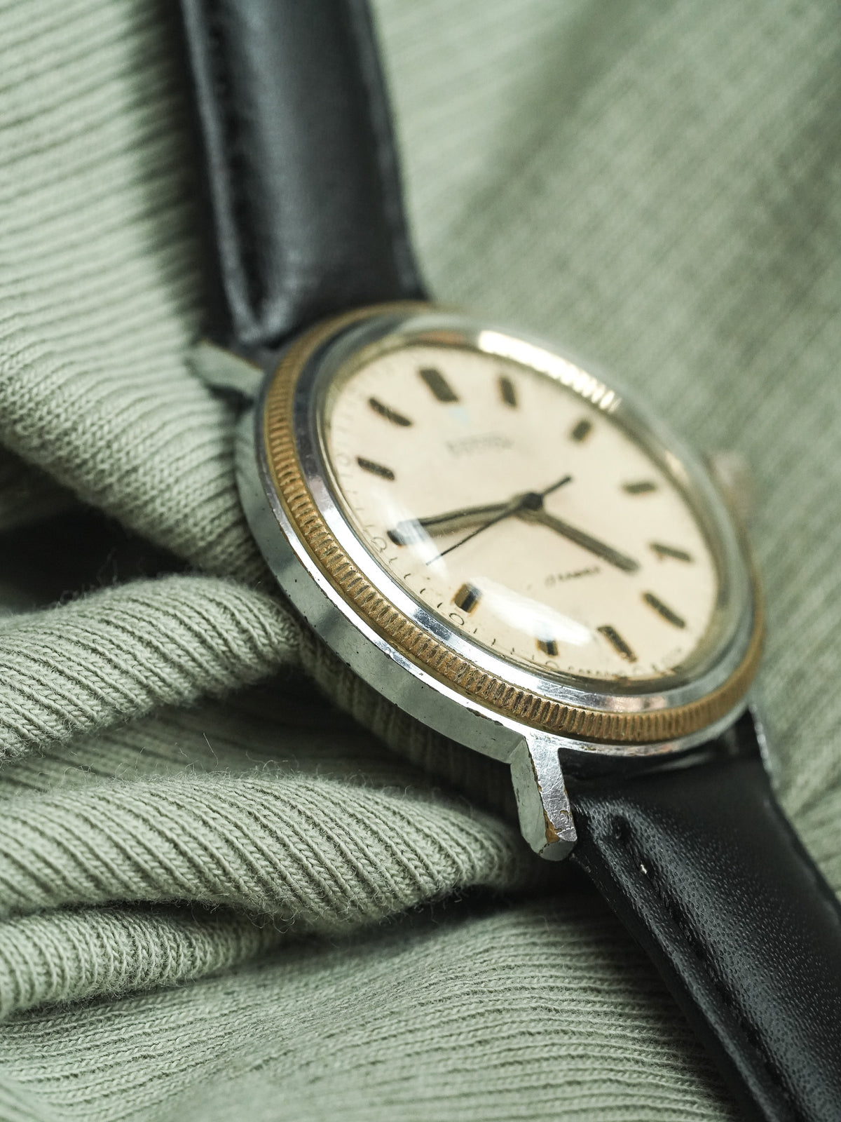 Vintage Omega watch with cream dial, gold bezel, black leather strap on green fabric