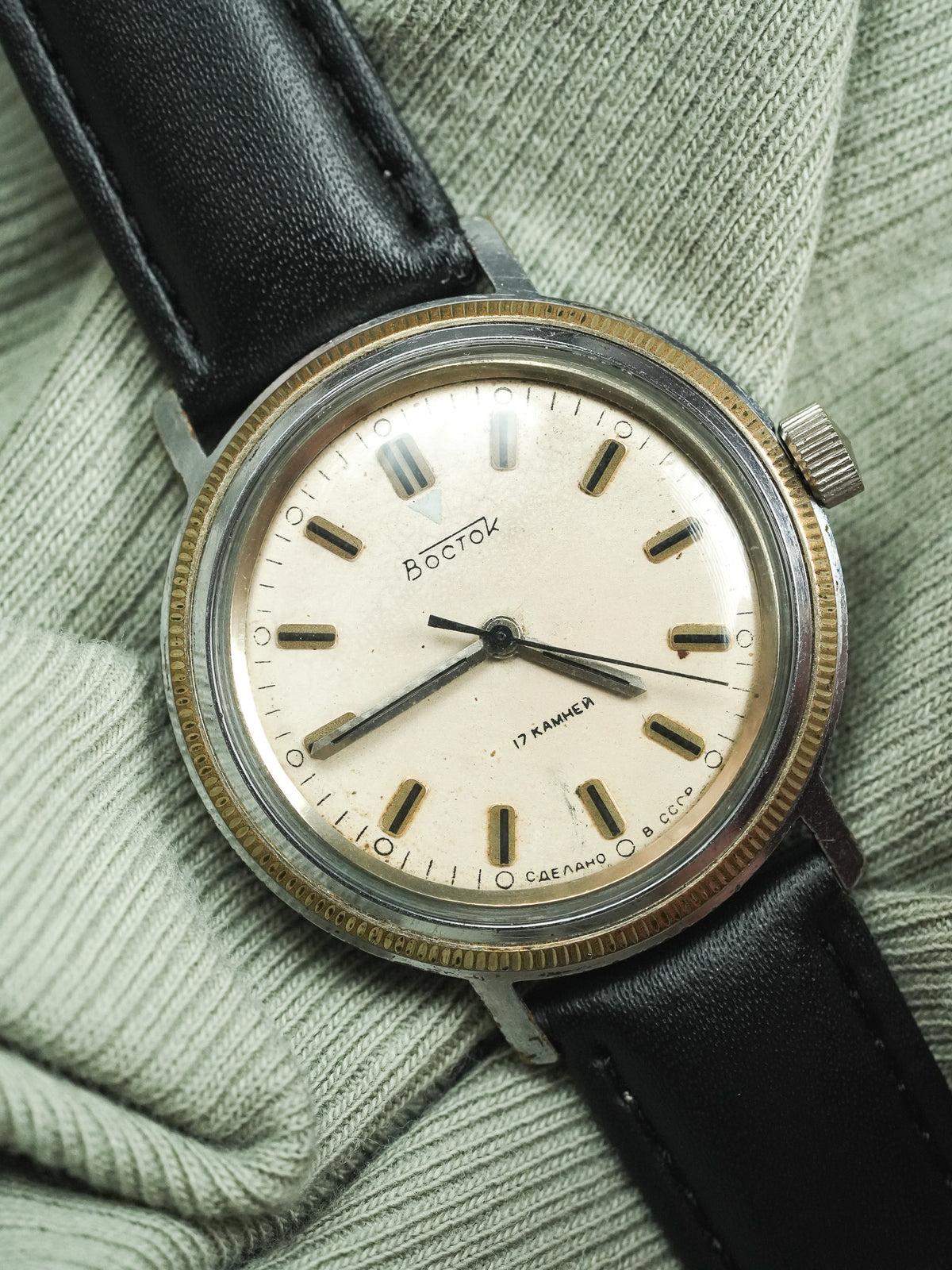 Vintage Vostok watch with cream dial, black leather strap, resting on green fabric