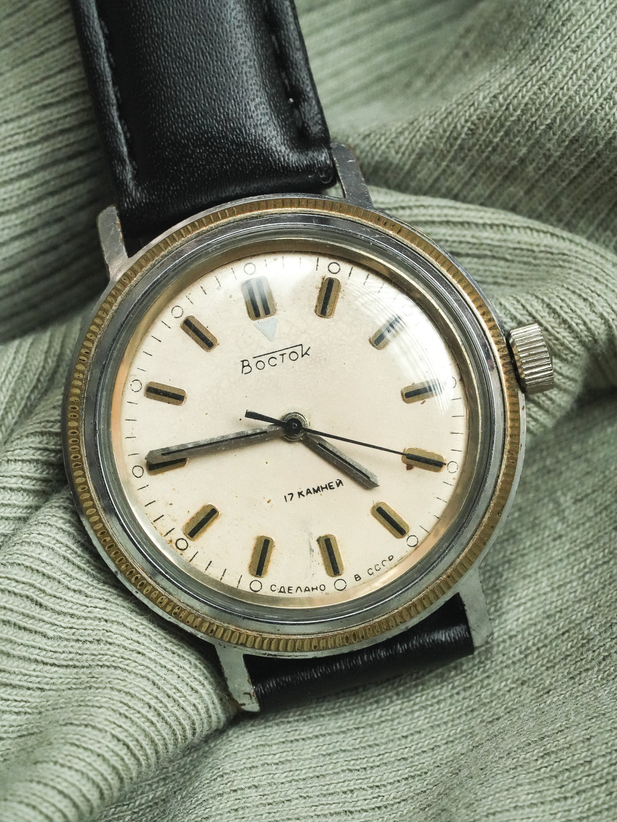 Vintage Vostok watch with cream dial, black leather strap, resting on green fabric