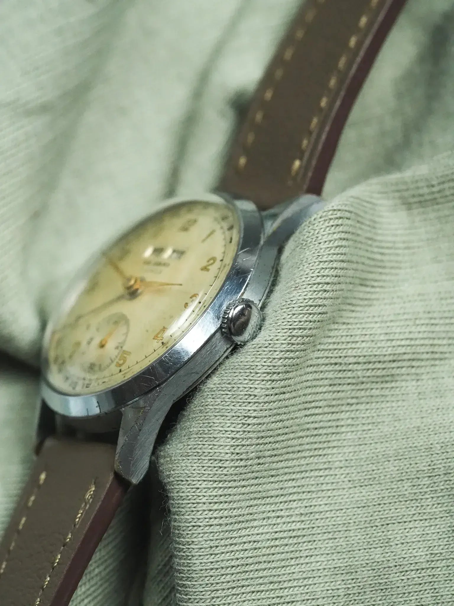Vintage Universal Genève watch with cream dial, steel case, brown leather strap on fabric