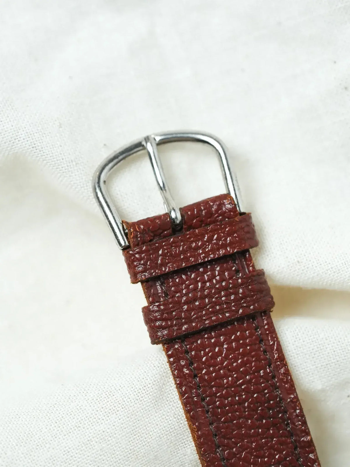 Vintage watch strap in burgundy textured leather with silver buckle on white fabric