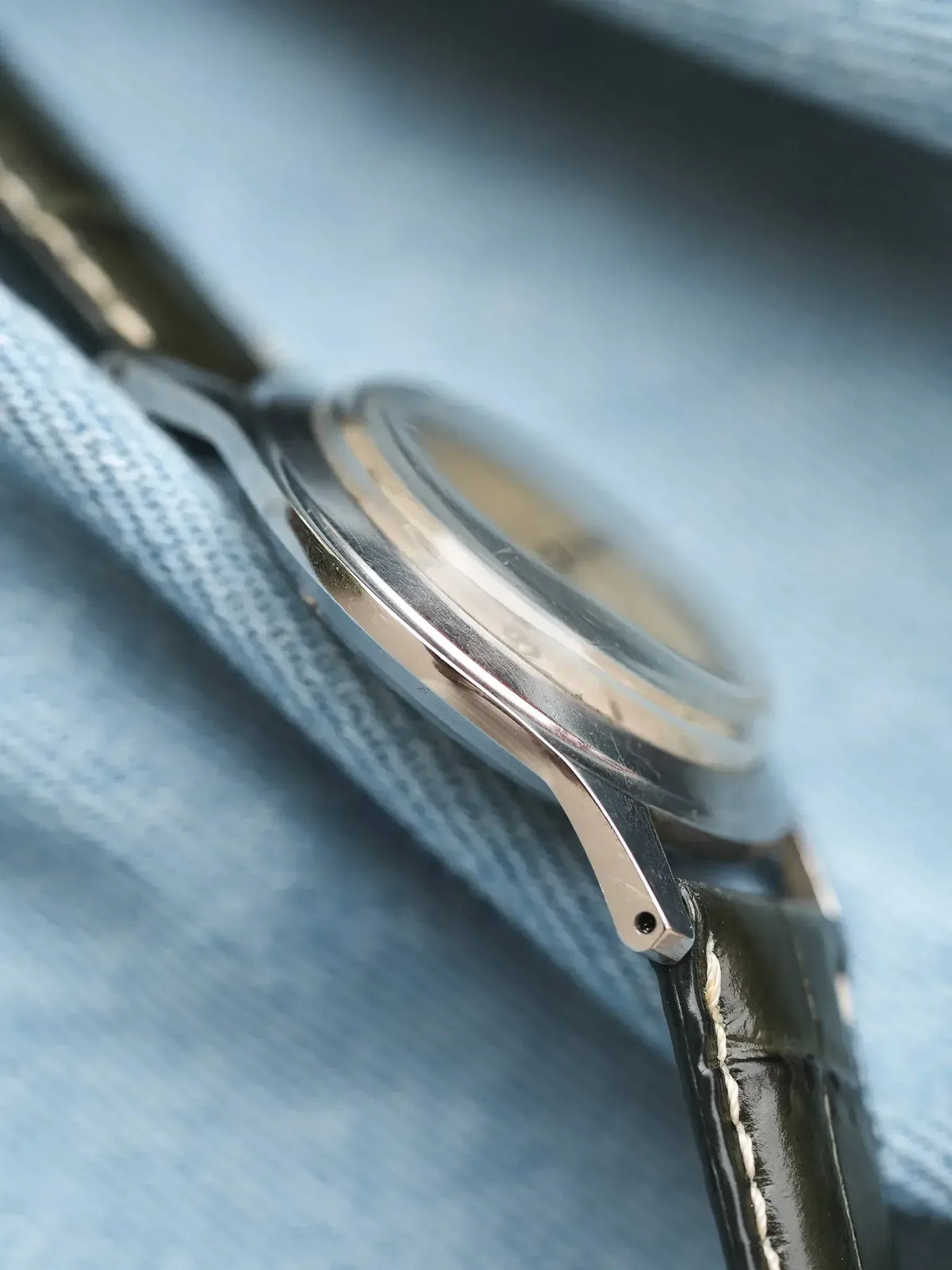 Vintage Omega watch with steel case and black leather strap on denim