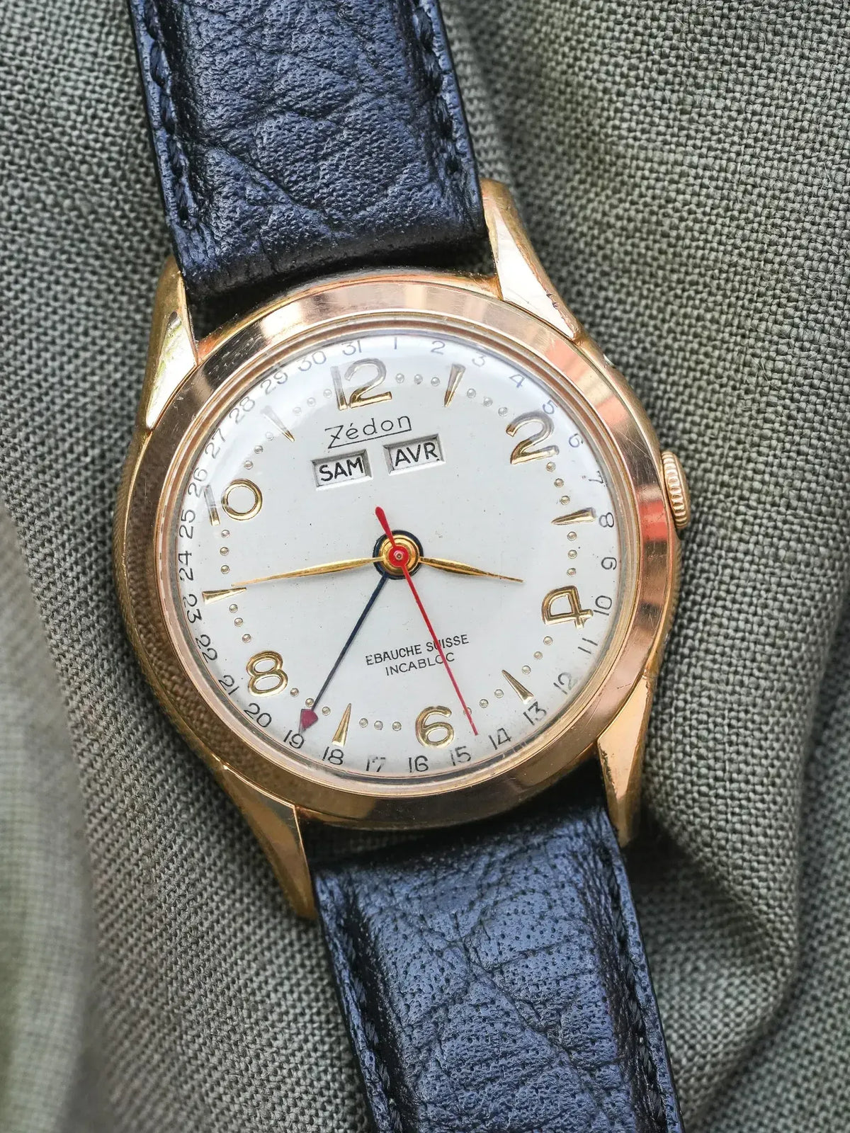 Zédon vintage watch with gold case, white dial, blue leather strap on fabric