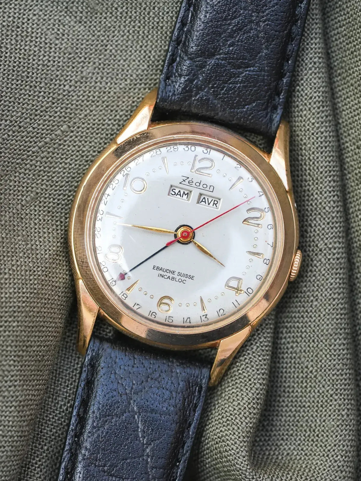 Zédon vintage watch with gold case, white dial, black leather strap on fabric