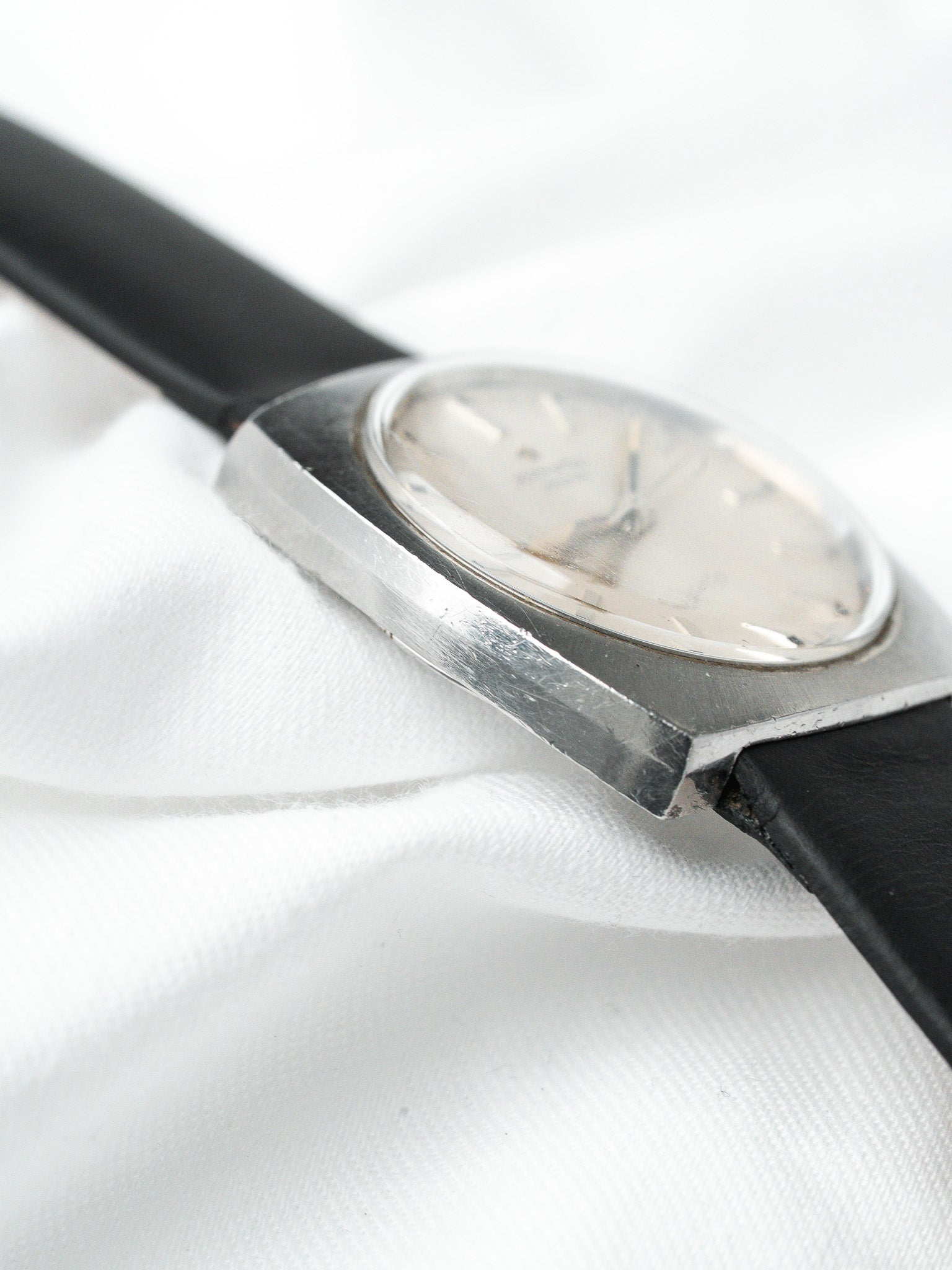 Vintage Omega watch with silver case, cream dial, black leather strap on white fabric