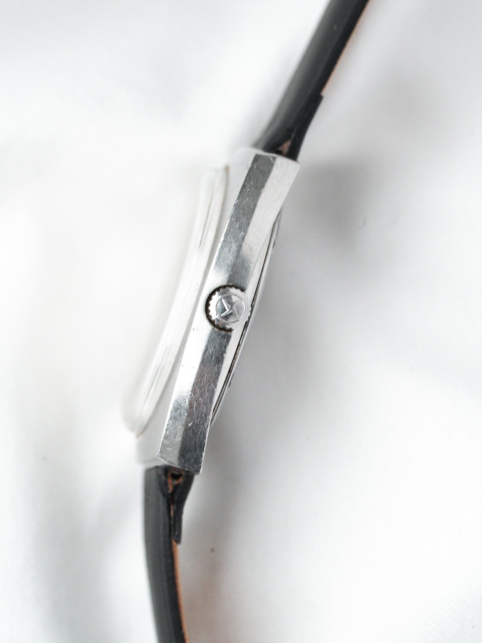 Vintage Omega watch side view, stainless steel case, black leather strap on white background